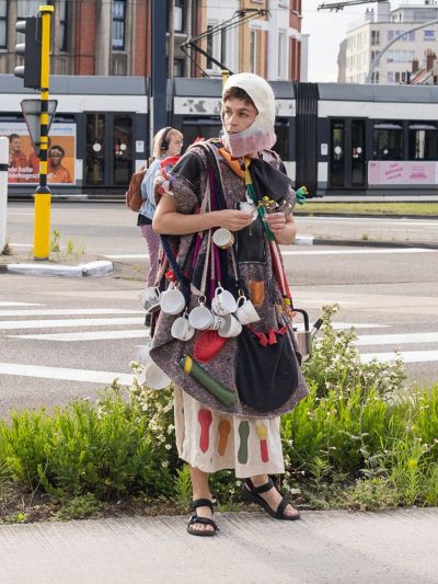 Pierre-Yves Delannoy, Willkommen bei den AGA (2024), performance participant wearing a handmade costume with cups and objects during a street performance.