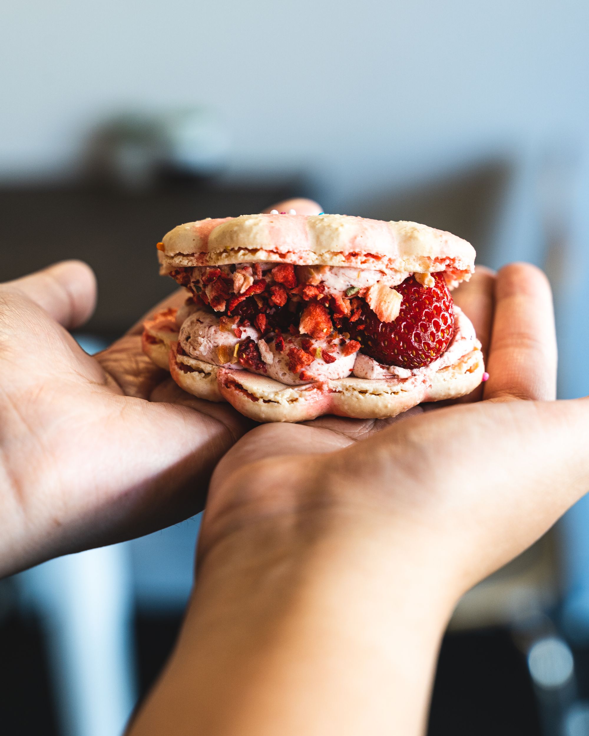 Close up view of a strawberry macaron being held in two hands