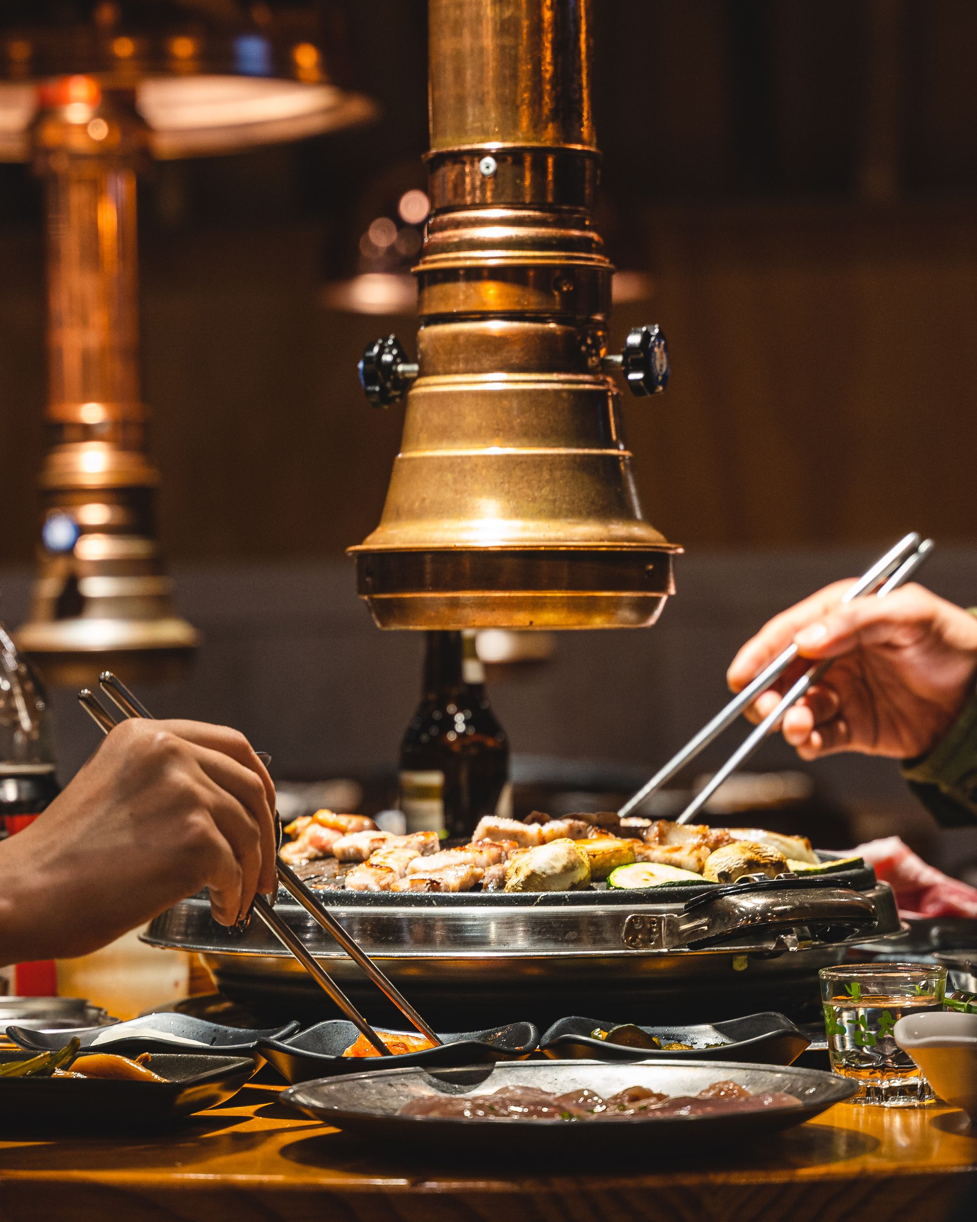 Close up shots of two hands picking food up from KBBQ grill