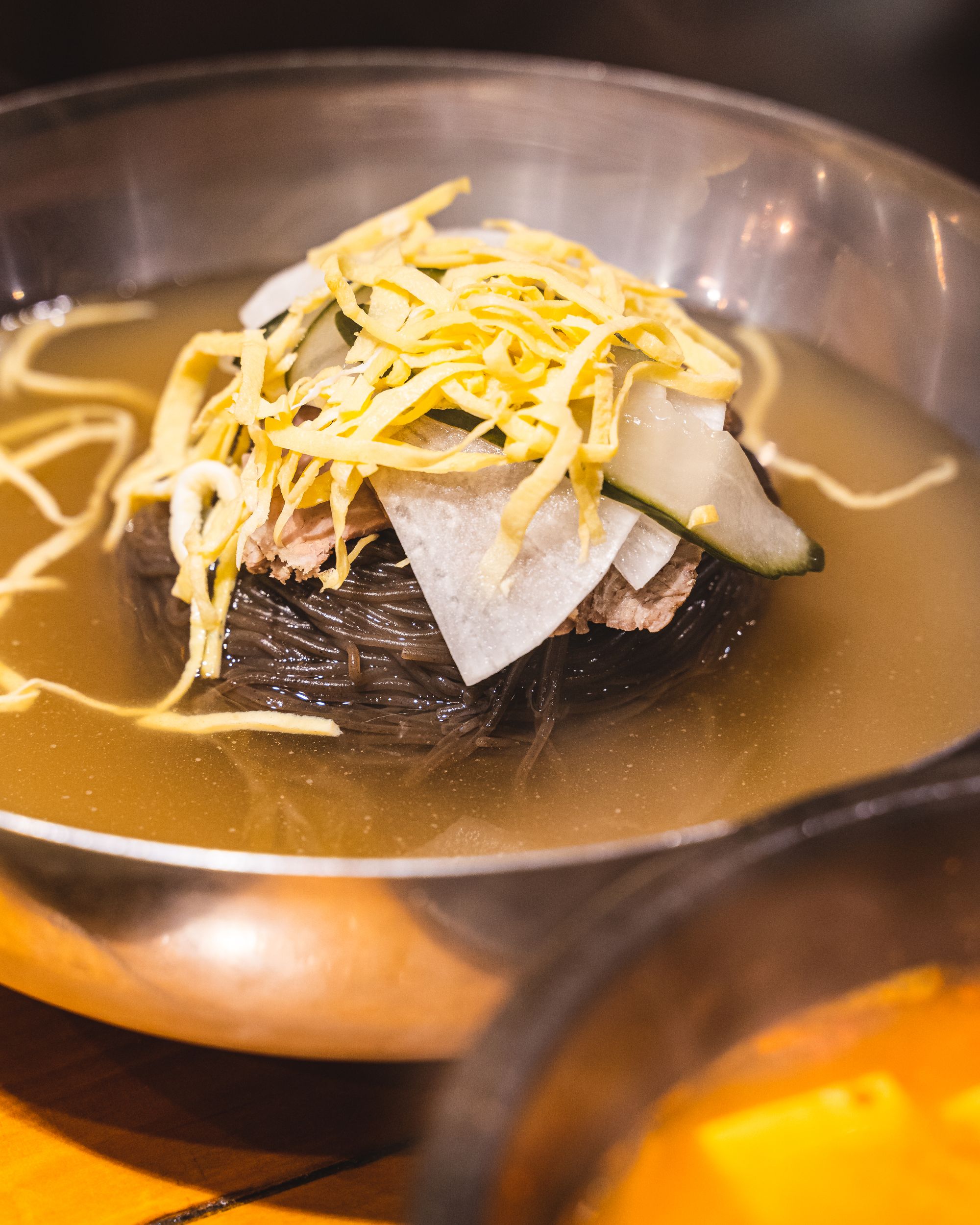 Close up shot of Korean cold noodles with black buckwheat noodles, sliced diakon and shredded egg on top