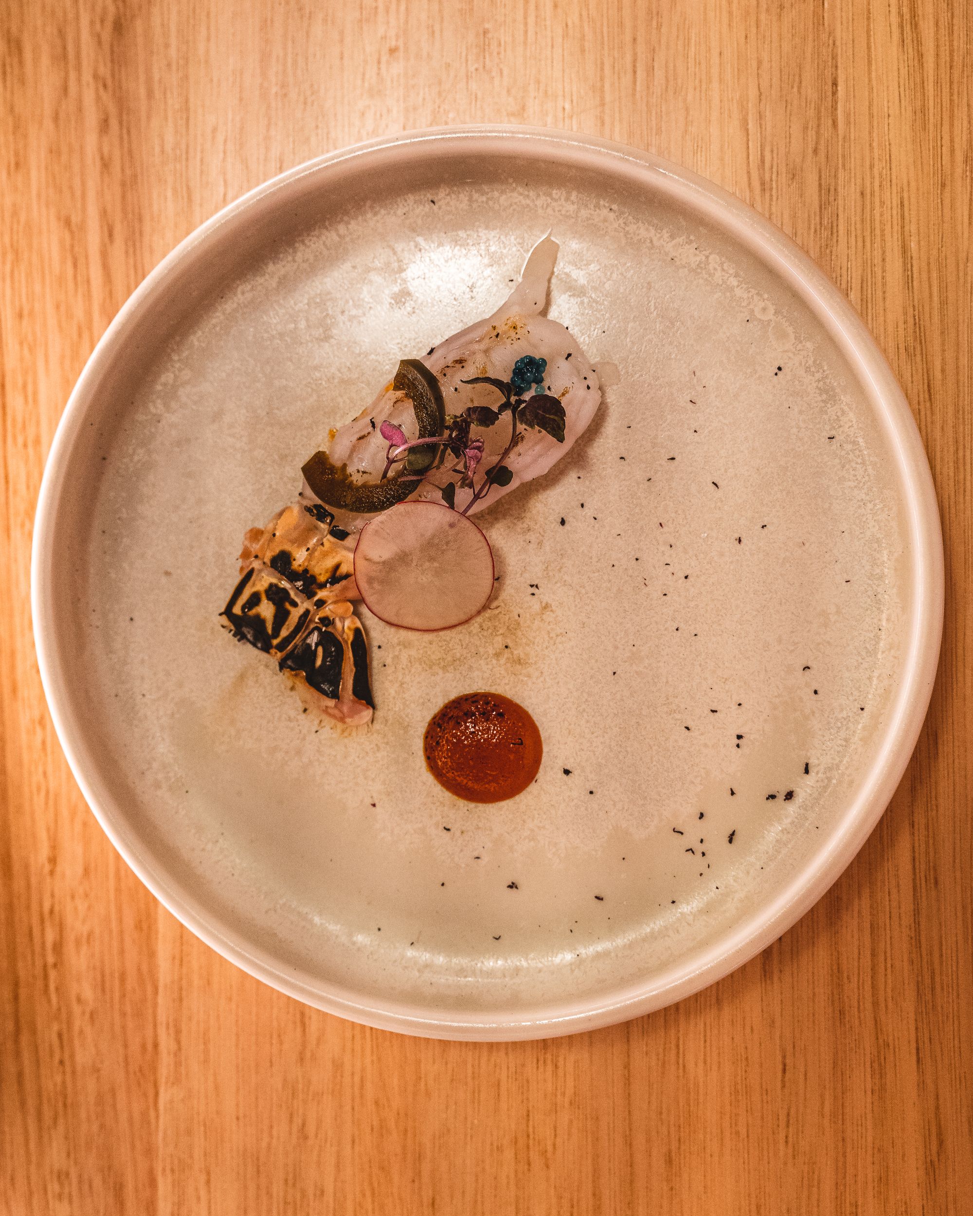 Top down shot of scampi with caviar on a plate with a dot of spicy miso sauce