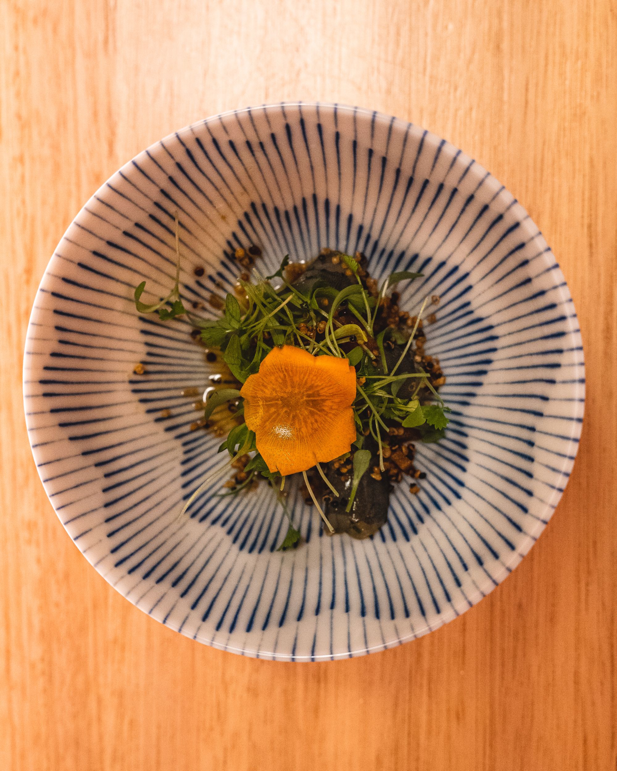 Top down shot of bowl with leafy greens and paradise prawns, topped with a delicately sliced carrot