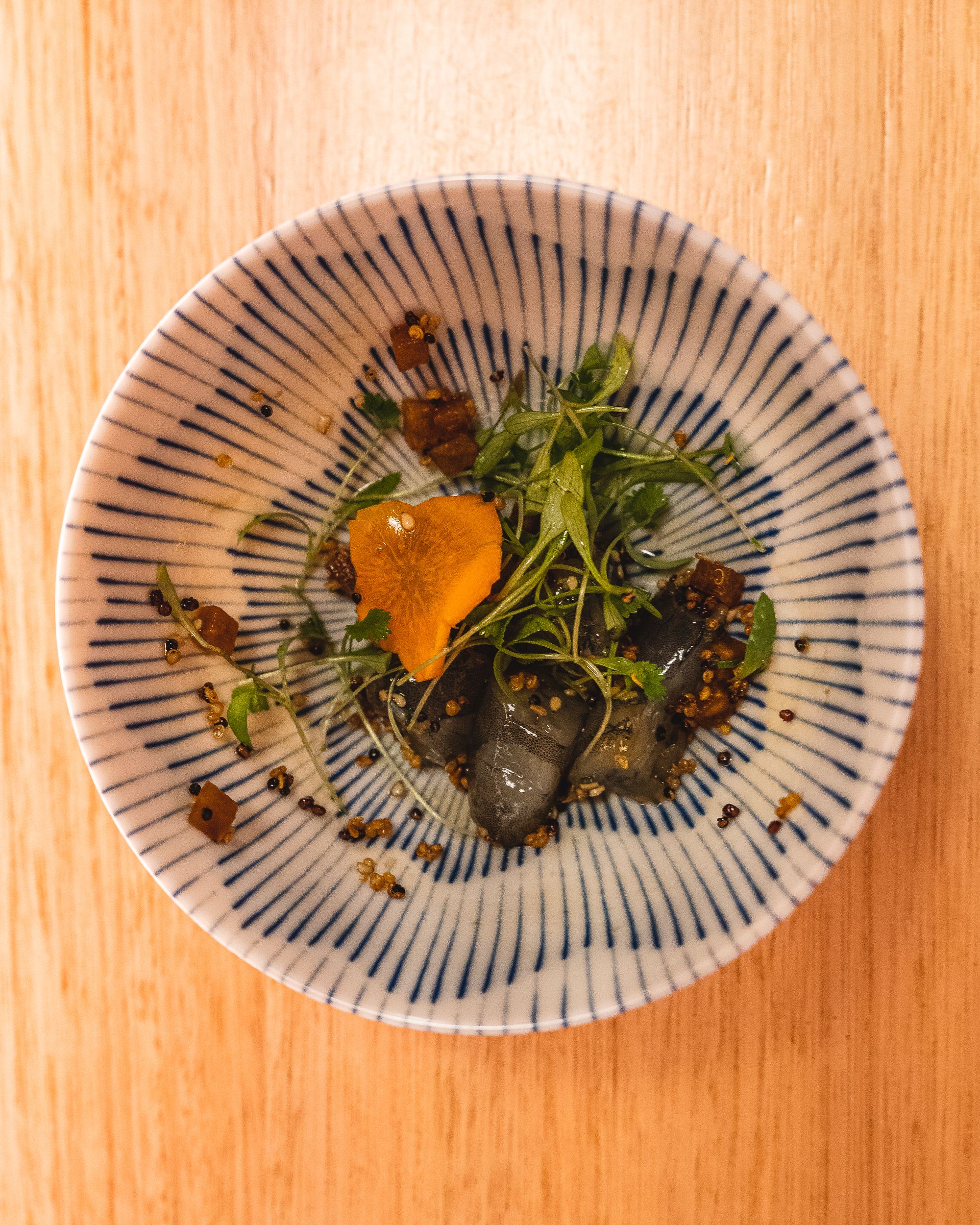 Top down shot of bowl with leafy greens and paradise prawns, topped with a delicately sliced carrot