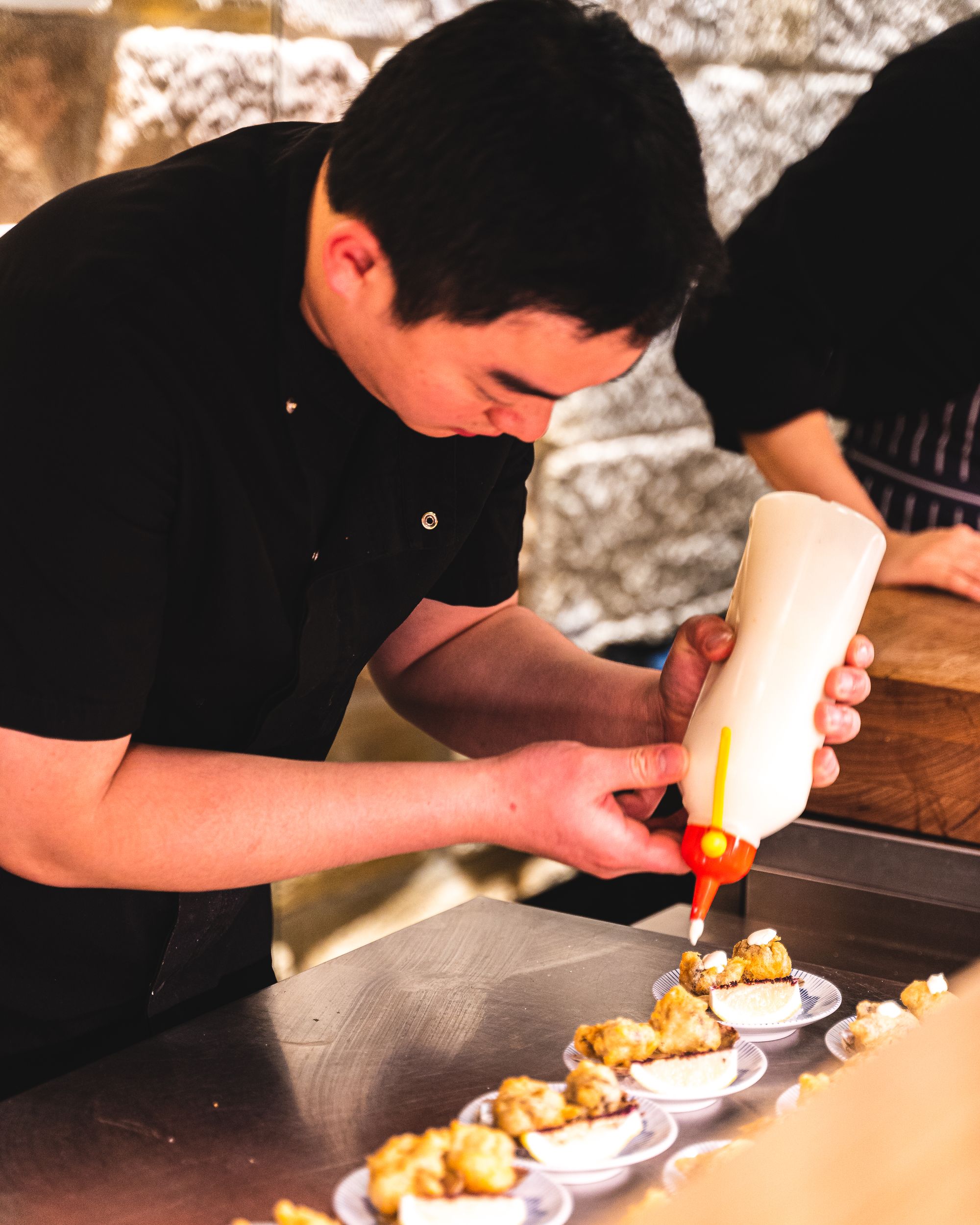 Asian chef squeeing wasabi yoghurt onto fried oysters