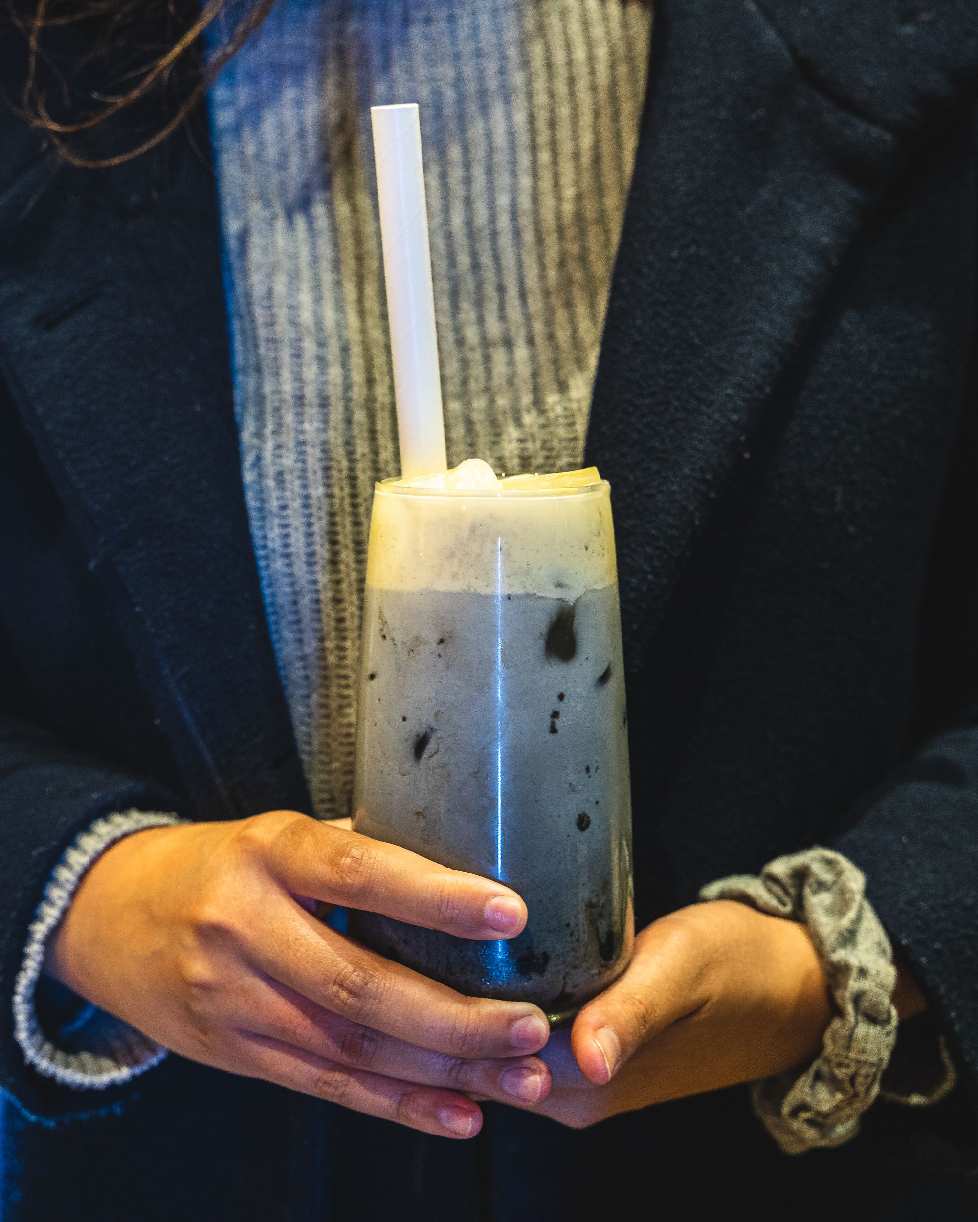 Hand holding a grey coloured drink with cream foam