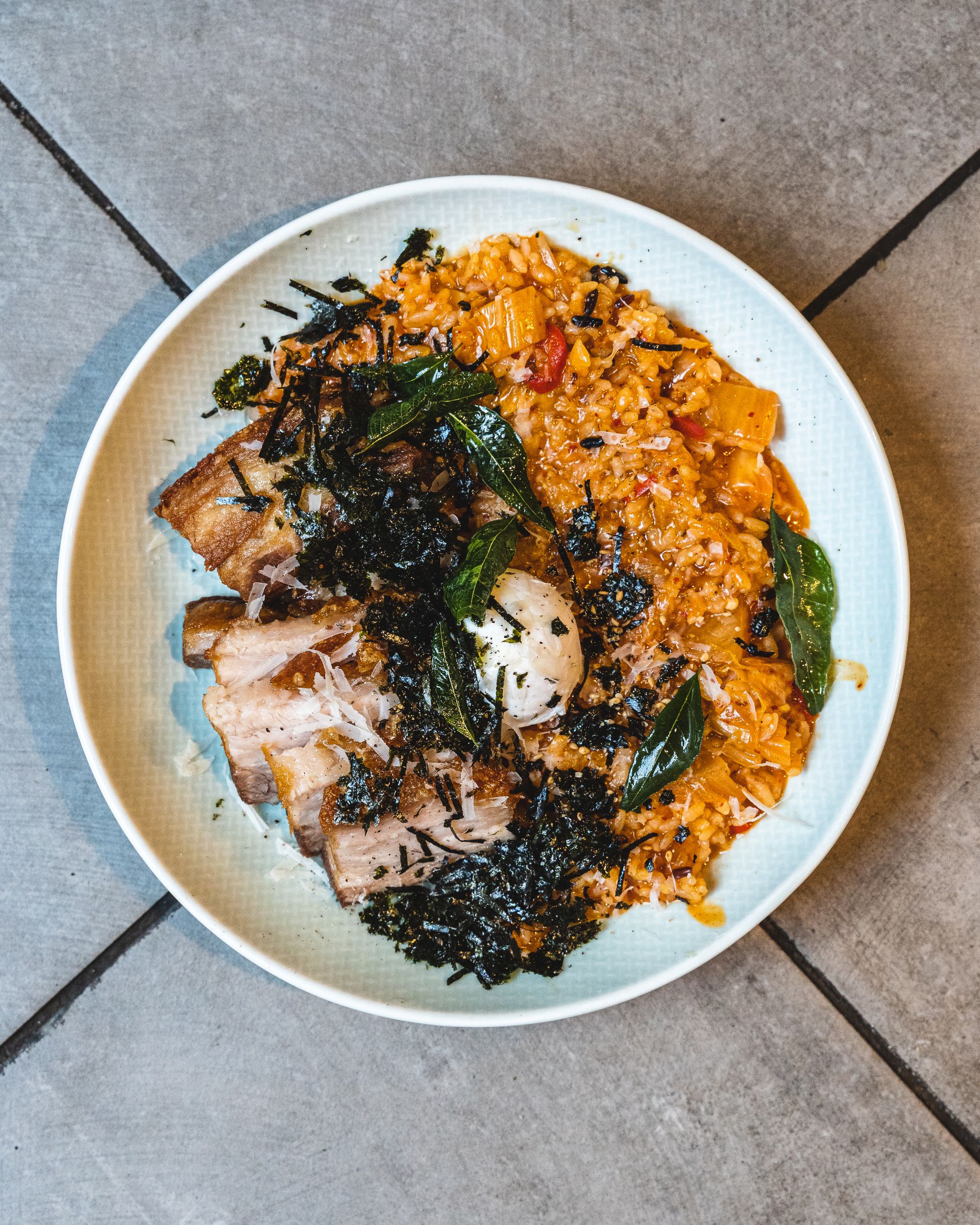 Overhead shot of risotto on a round plate with a poached egg and crispy pork belly