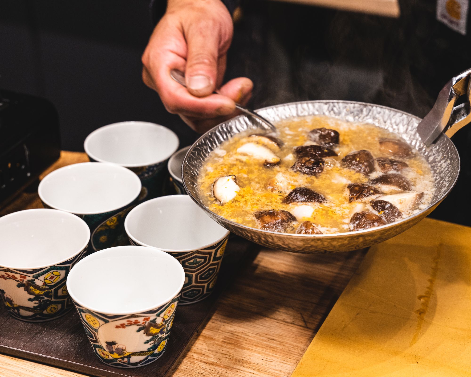 Hand holding a saucer pouring soup into soup bowls