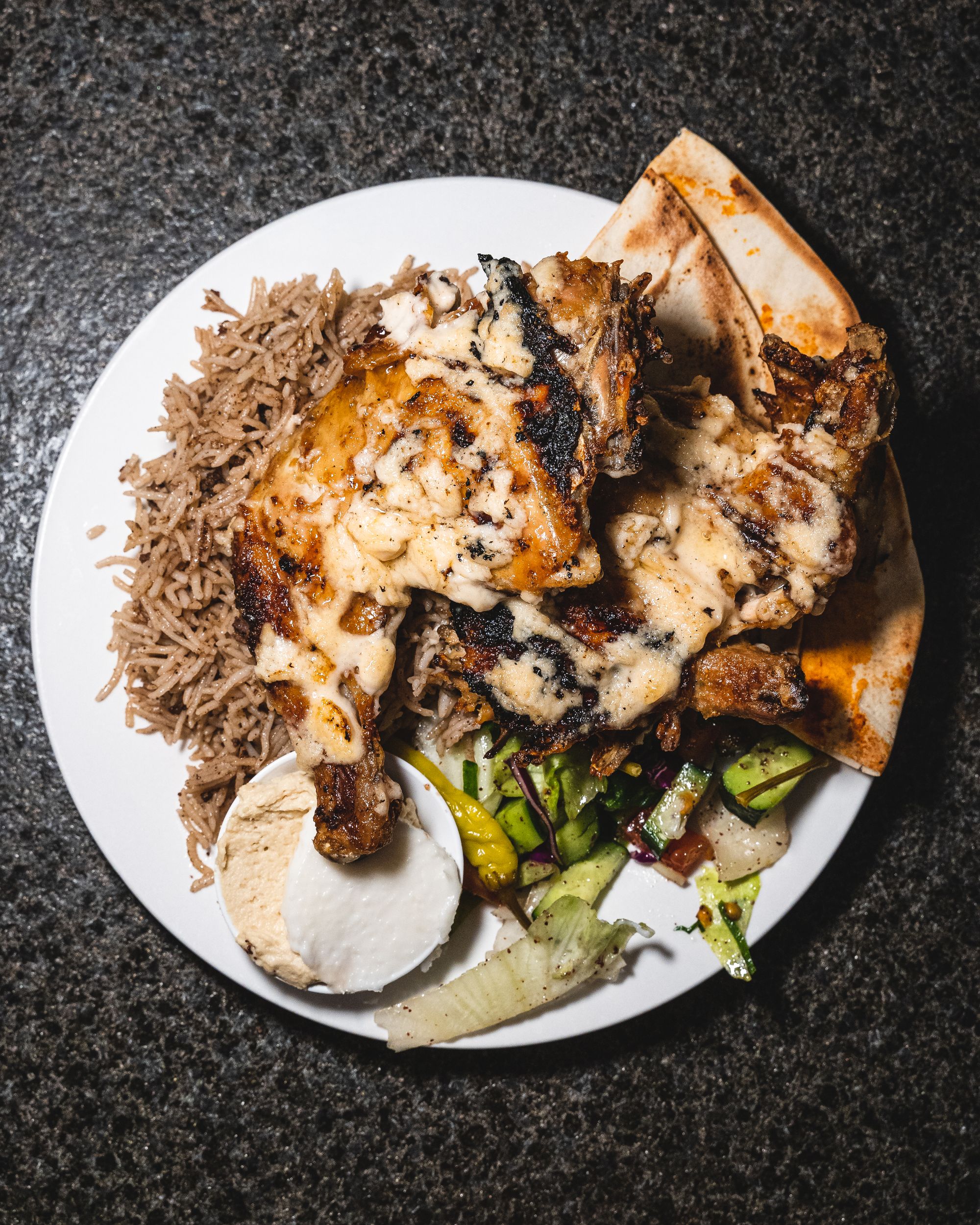 Top down shot of rice, hummus, pita bread, salad and charcoal chicken