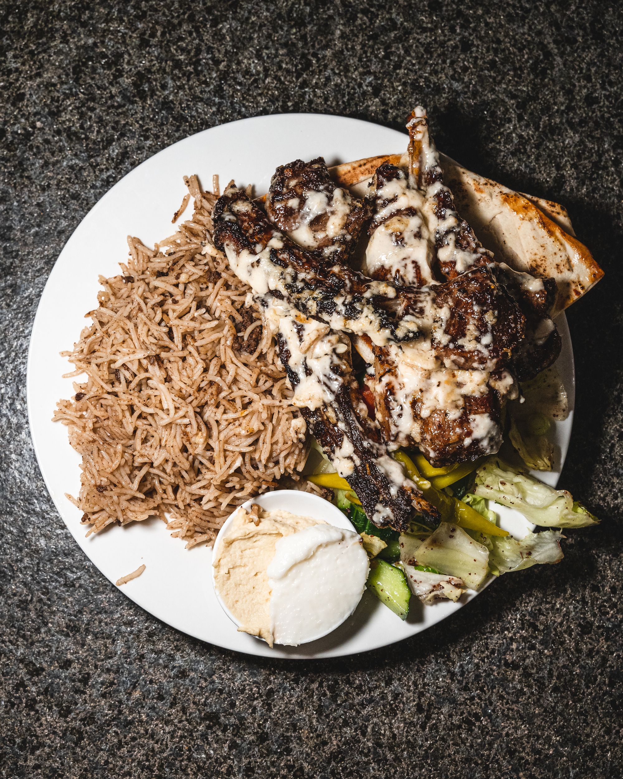 Top down shot of rice, hummus, pita bread, salad and lamb cutlets
