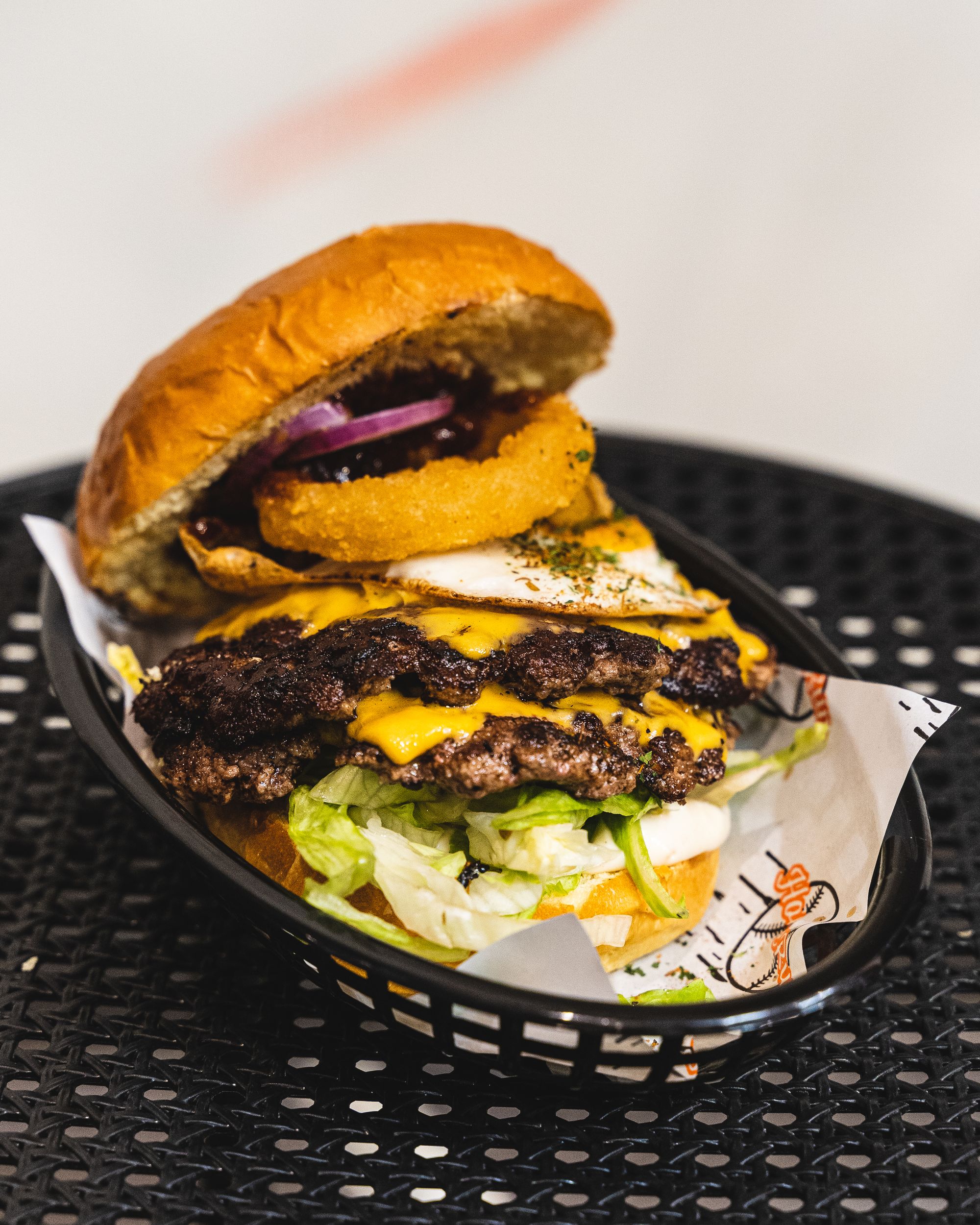Close up of large burger with two beef patties, cheese, onion ring, egg, onion and lettuce showing
