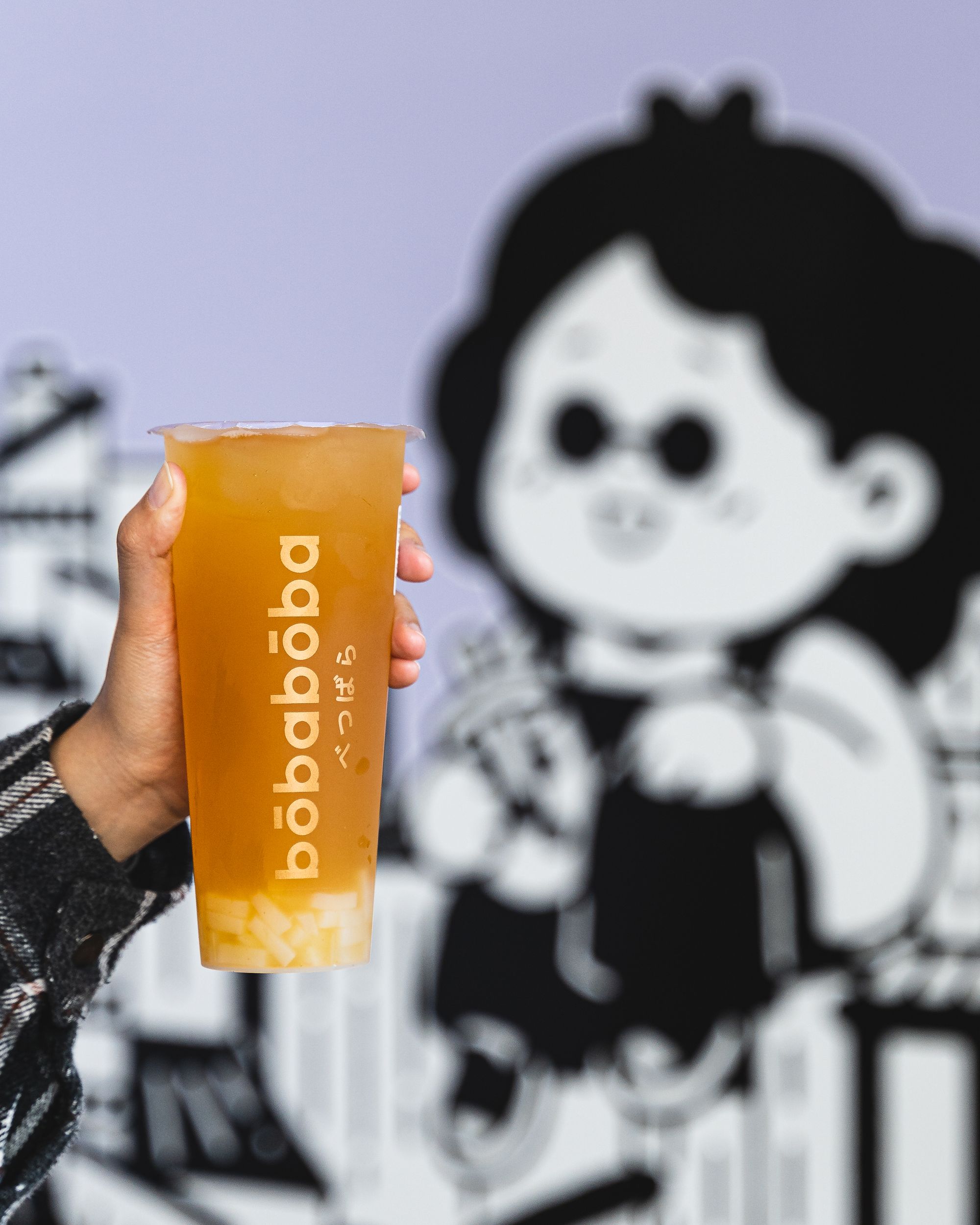 Hand holding up a orange coloured boba with lychee jelly