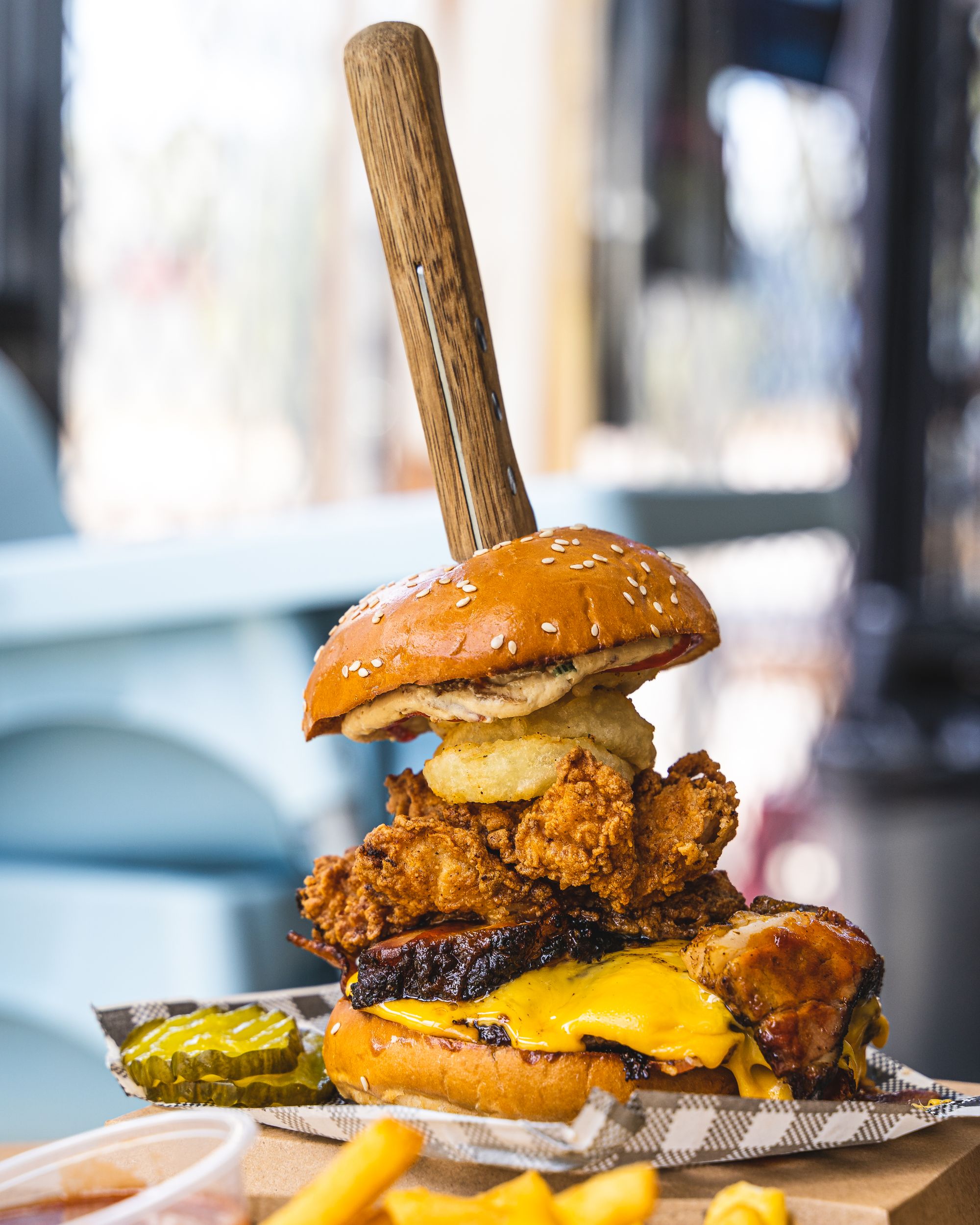 Close up of a burger with pork belly, fried chicken, onion ring and beef patty