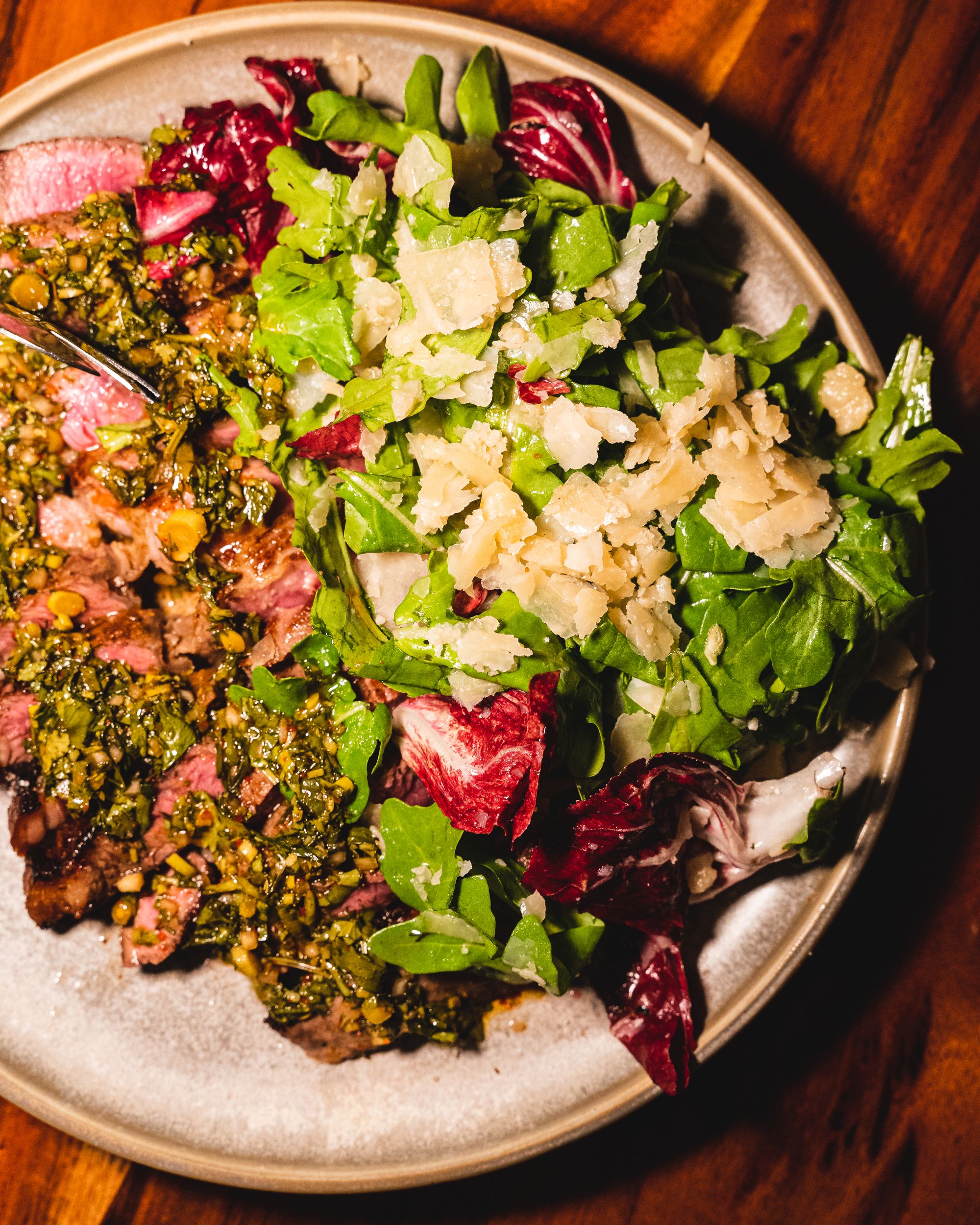Top down of steak with salsa verde, roquette and parmesan
