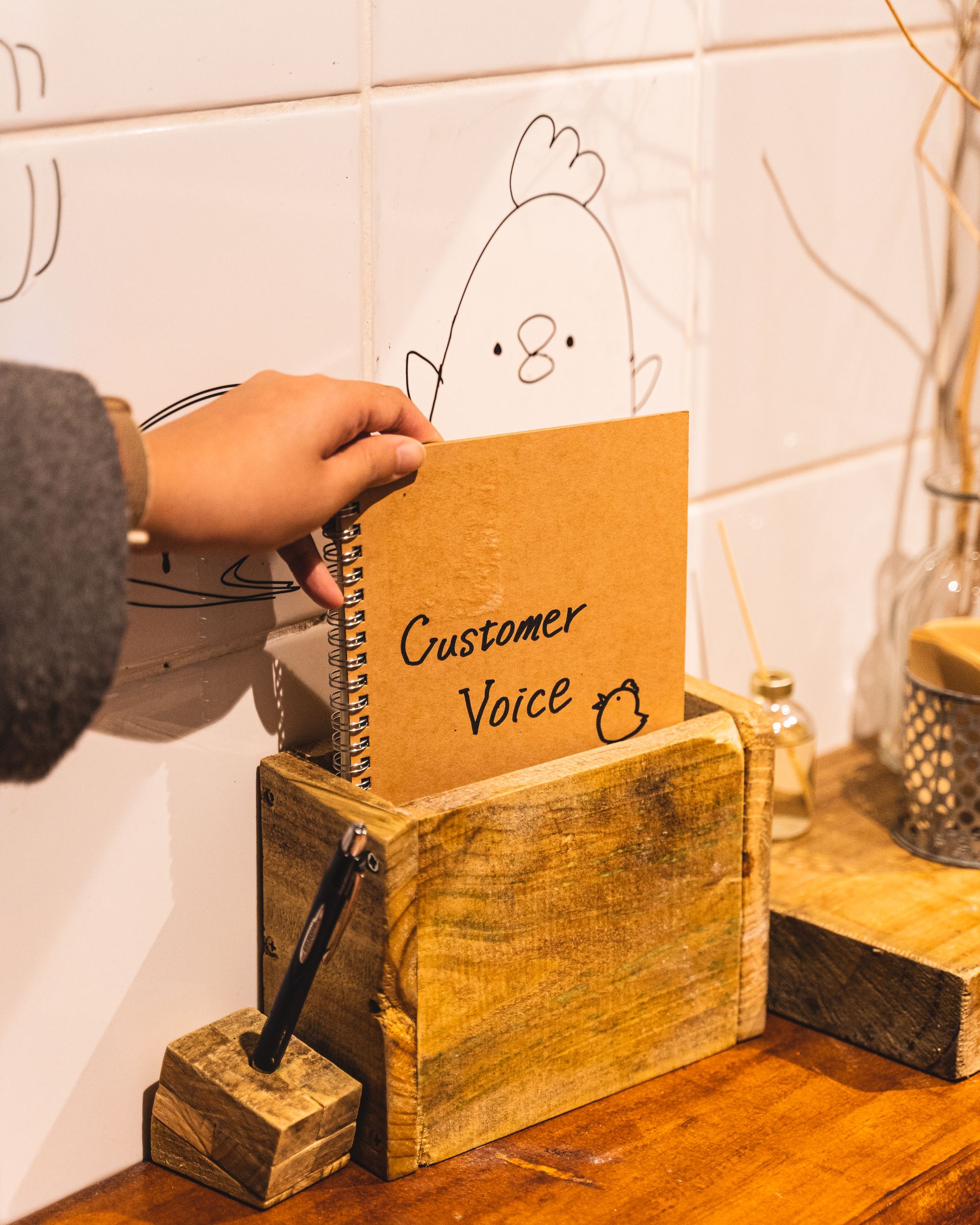 Hand holding a ring binder with "customer voice" written on the front and a cute bird drawn on it