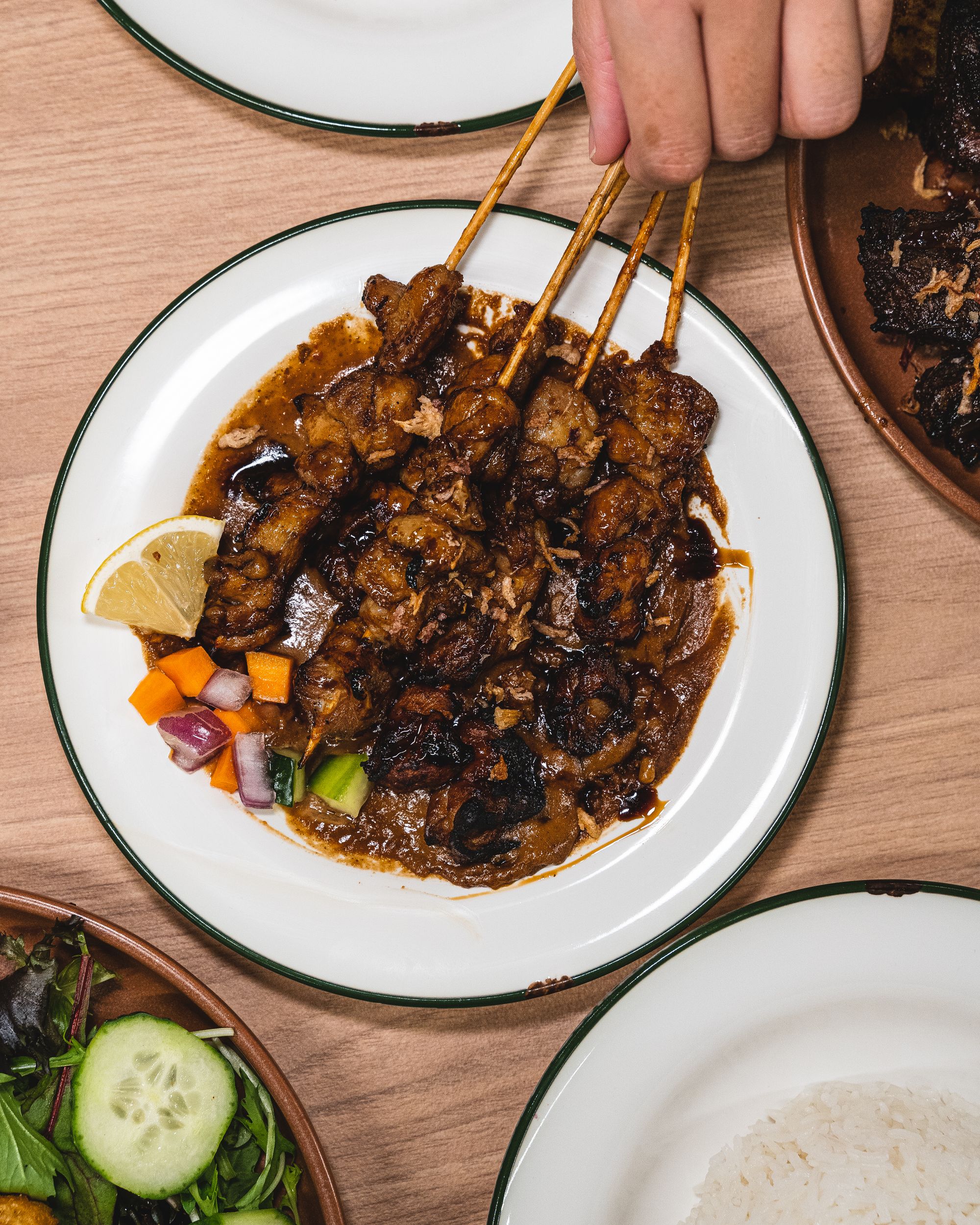 Top down of hand picking up chicken satay
