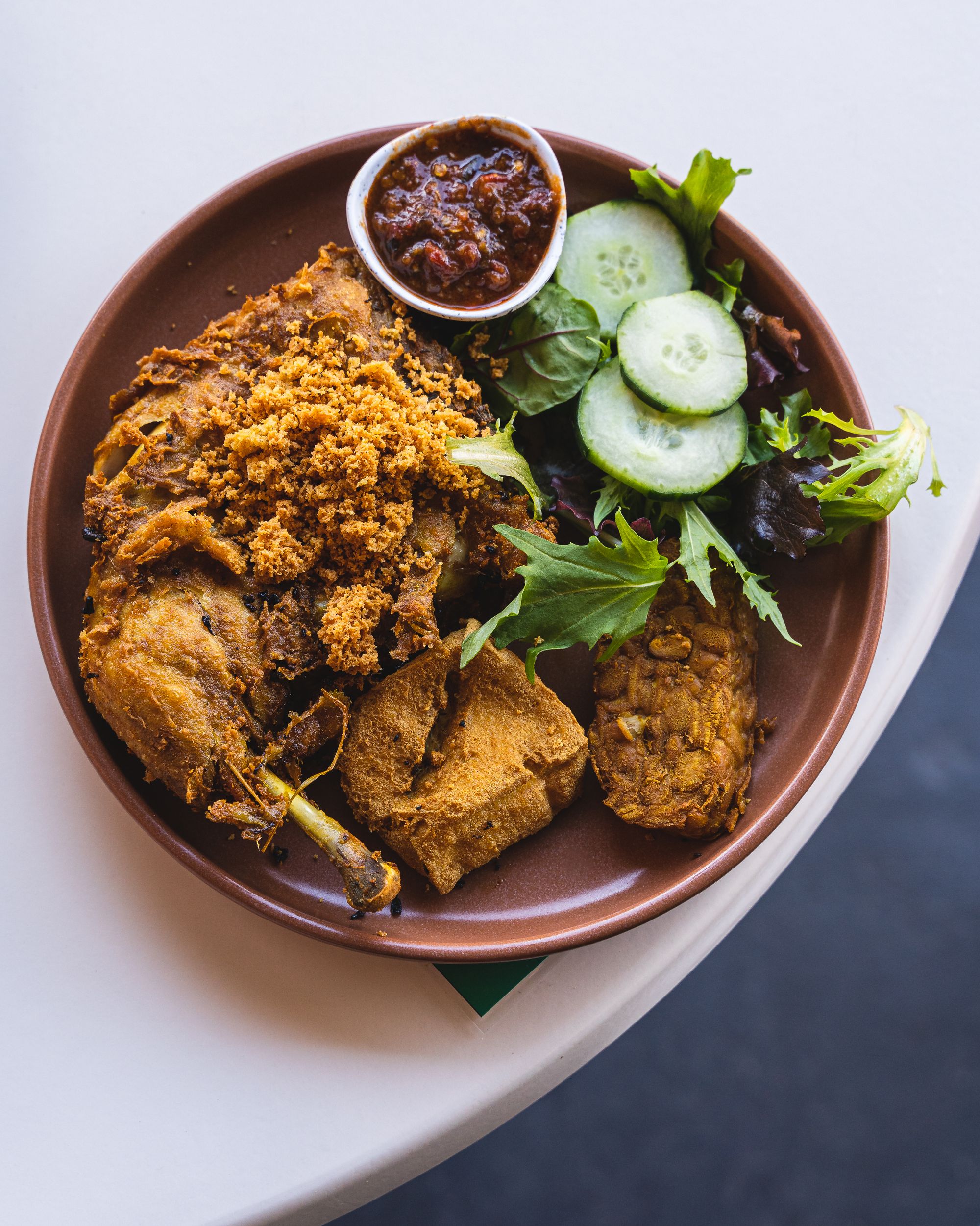 Top down of Indonesian fried chicken, tempeh, tofu, vegetables and sambal
