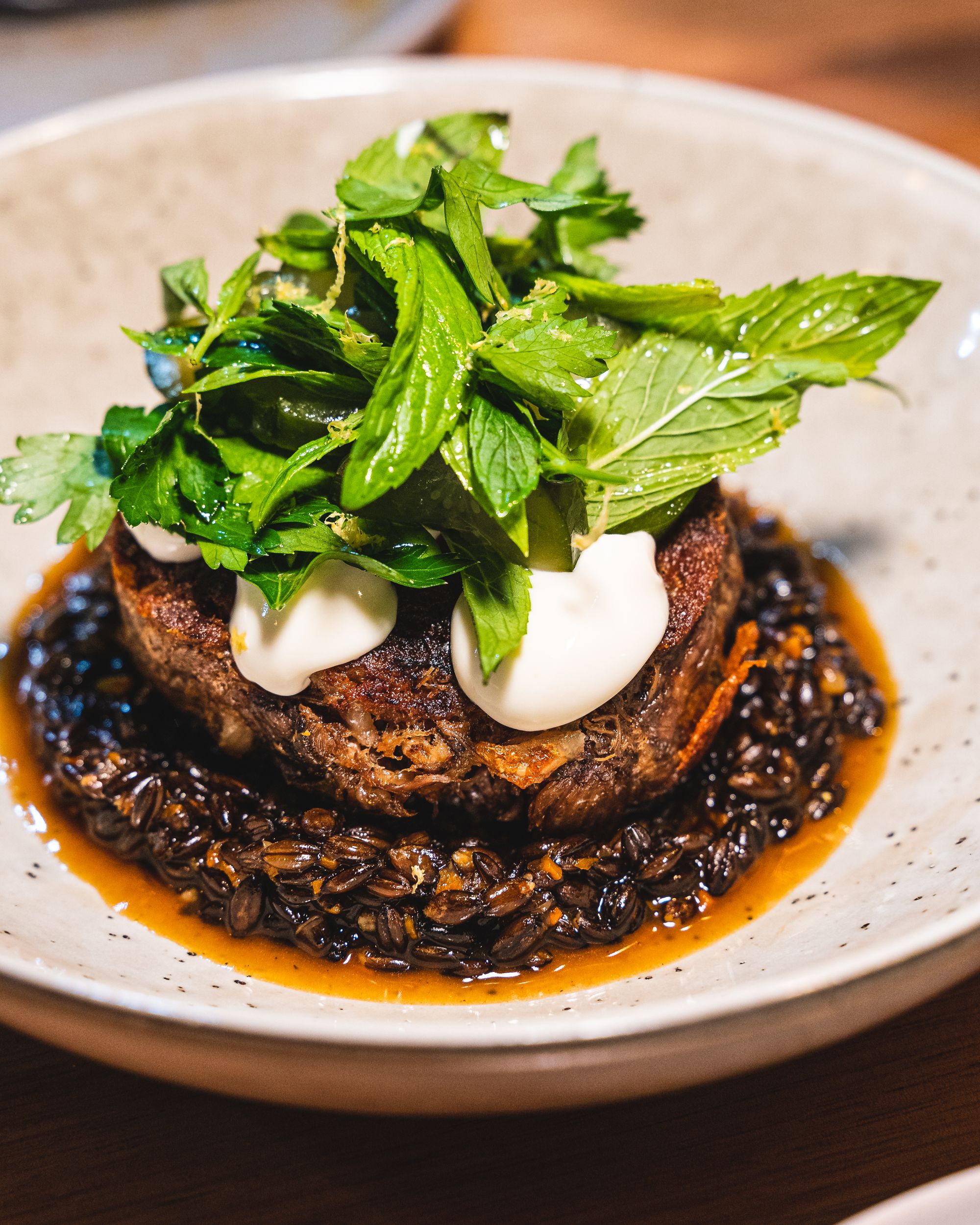 Close up of lamb topped with greens, ricotta and a moat of black barley