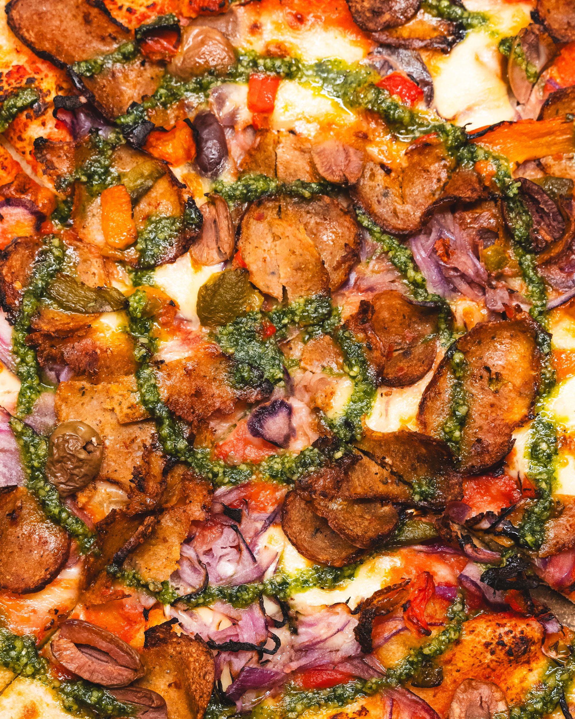 Top down shot of pizza with olives, pesto, red onion and roast capsicum