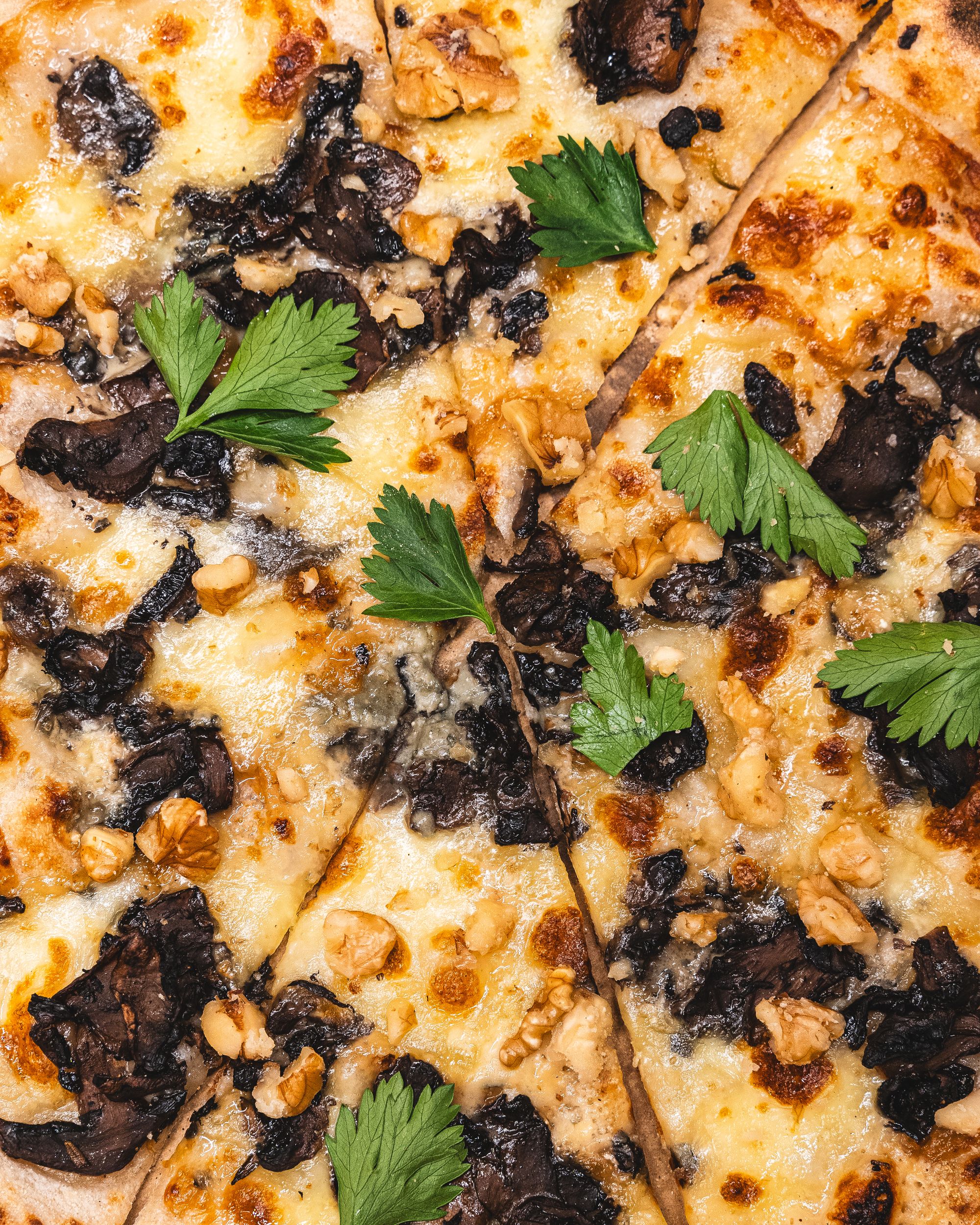 Close up of pizza with fior di latte, blue cheese, mushrooms, walnuts and parsley