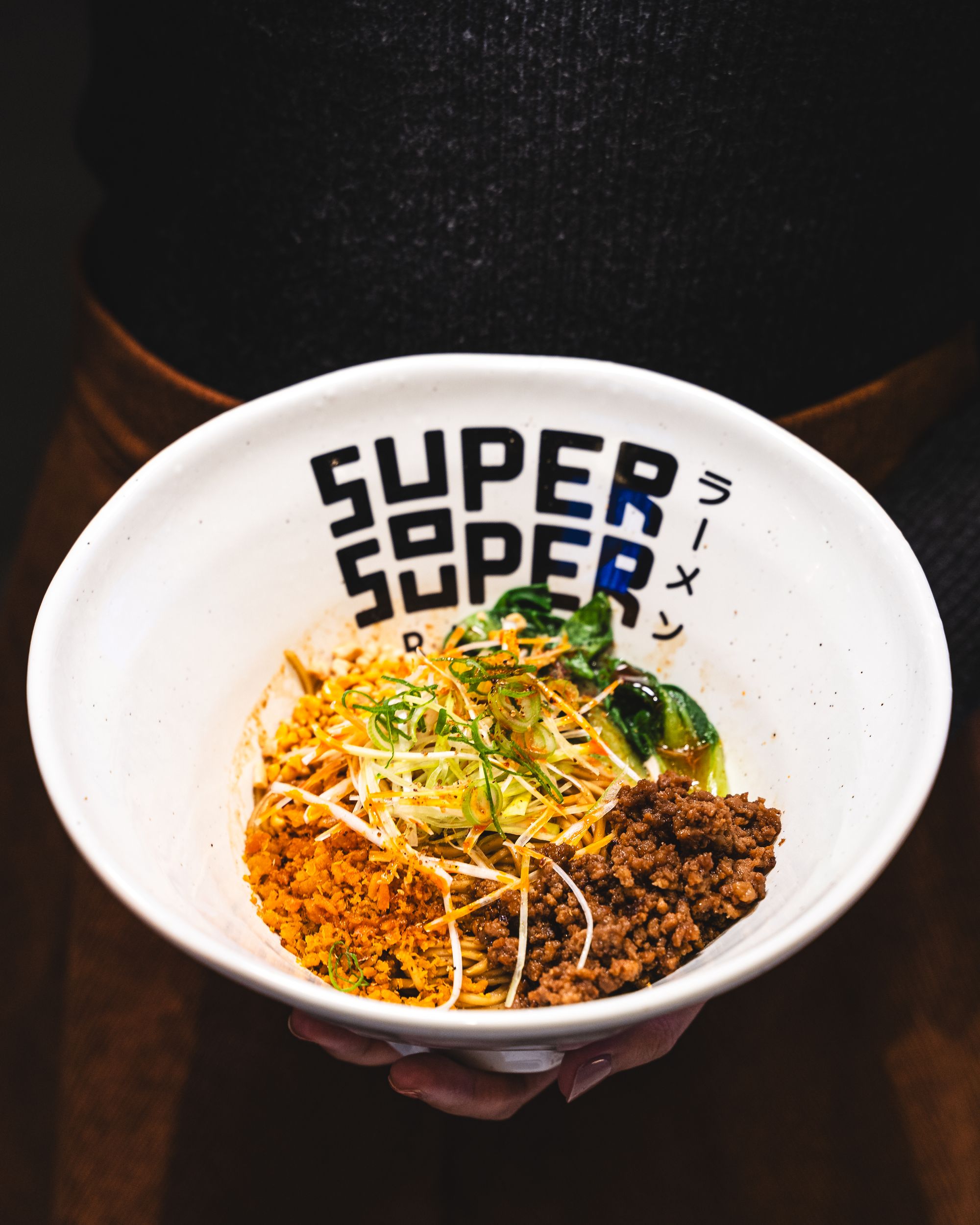 Close up shot of hand holding a bowl of tan-tan ramen with minced pork, peanuts and nori garnish