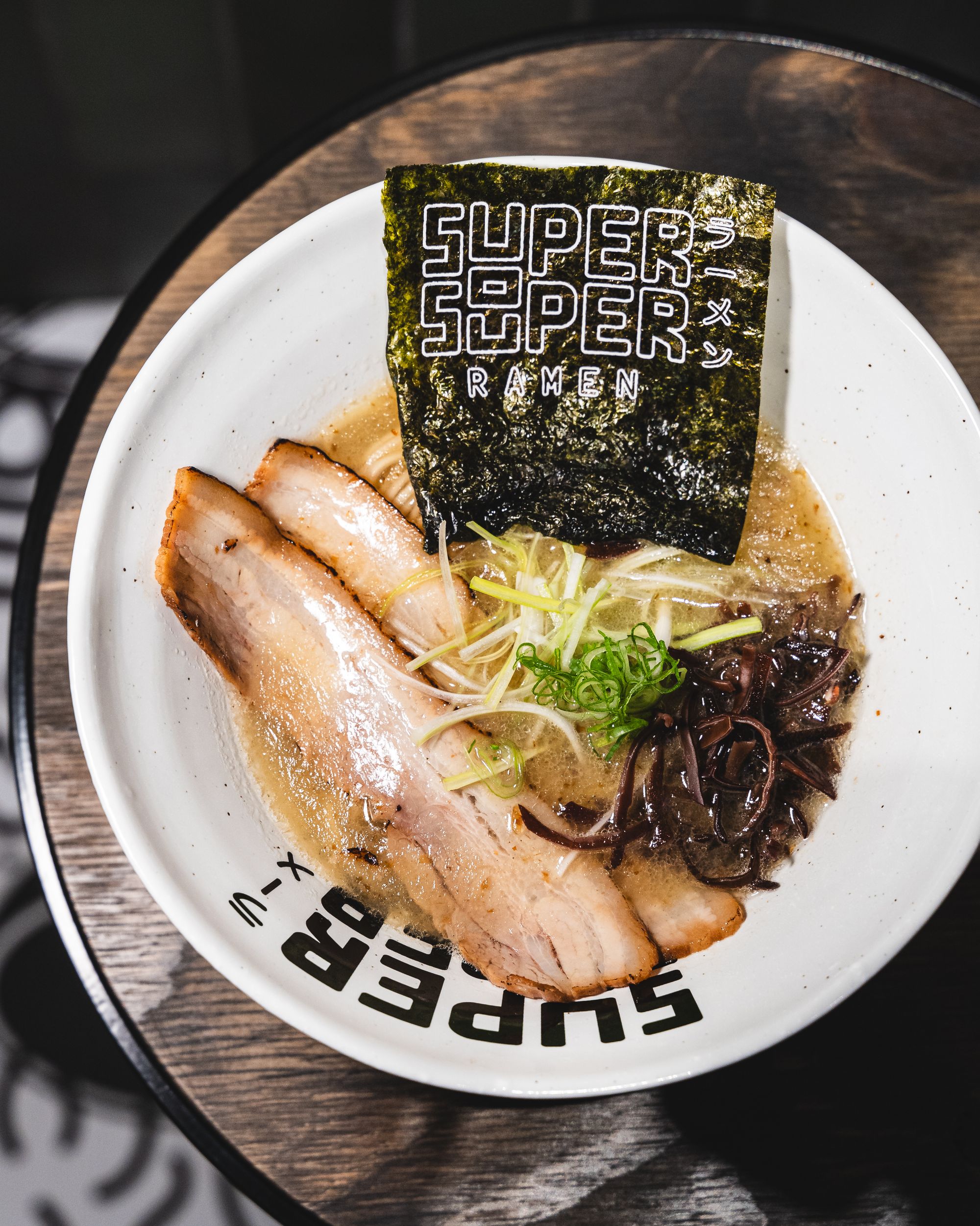 Top down shot of ramen bowl with chashu, seaweed, nori and scallions 