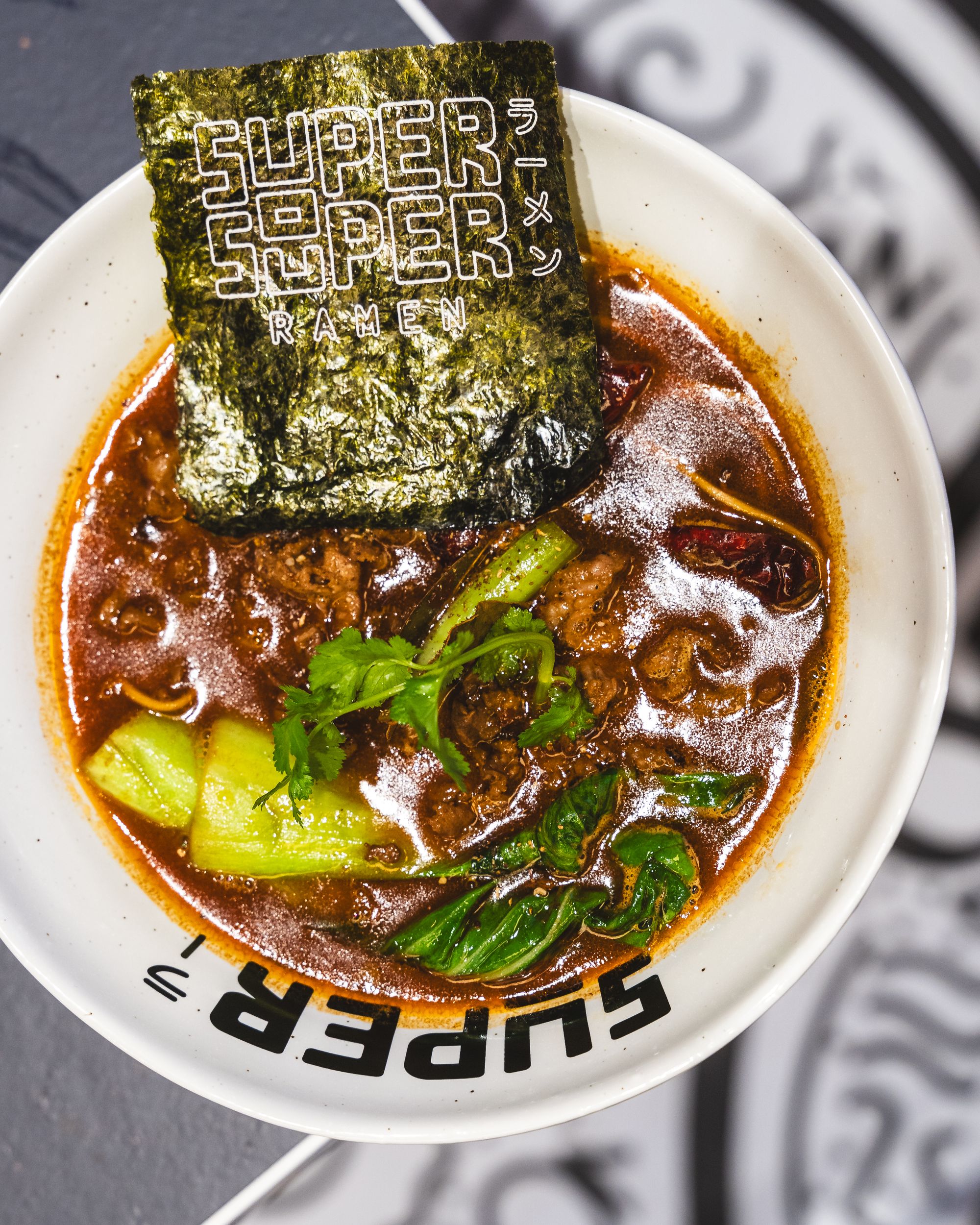 Top down shot of ramen with bok choy, nori, coriander and beef slices
