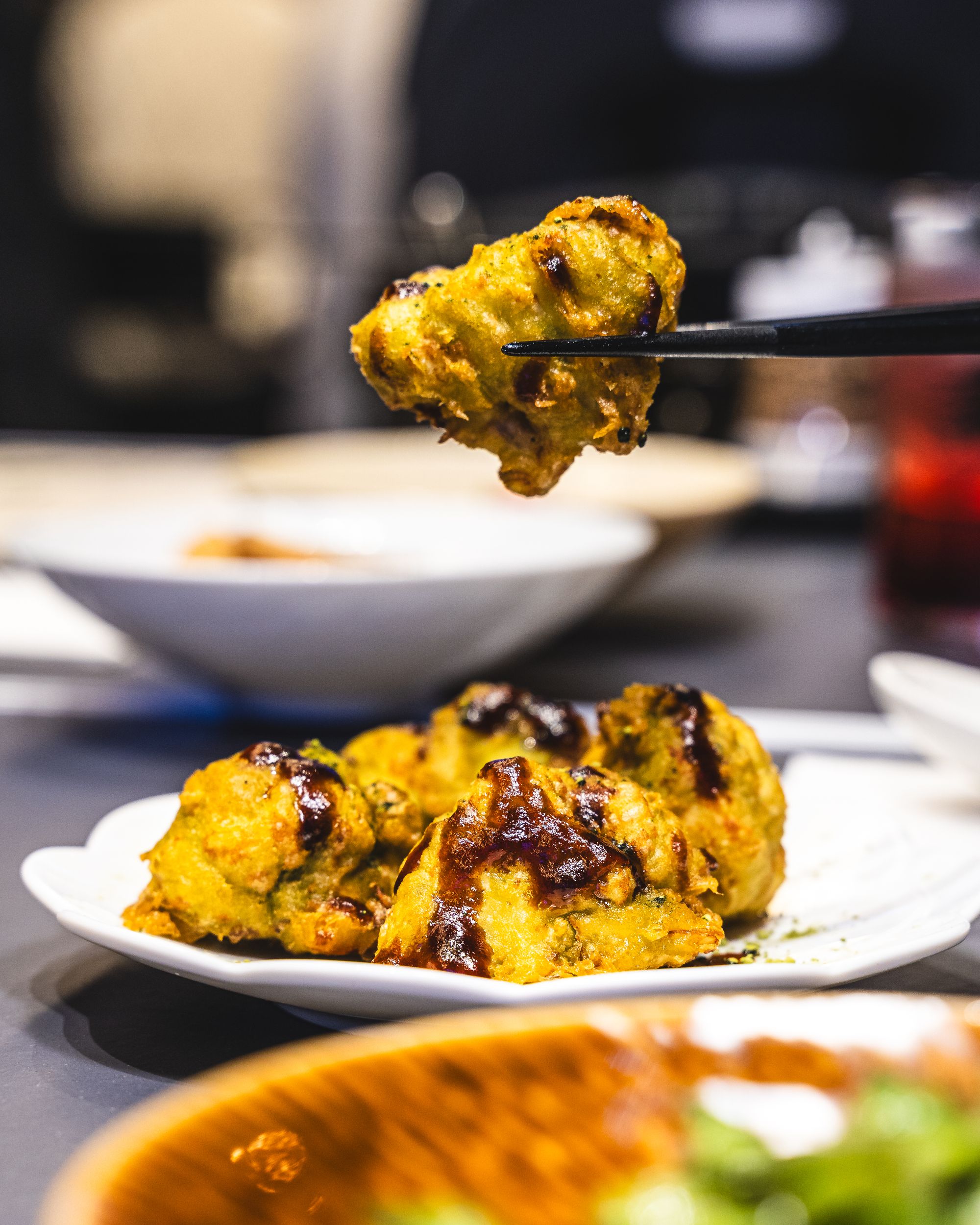 Fried cauliflower pieces with black vinegar glaze being held up with chopsticks
