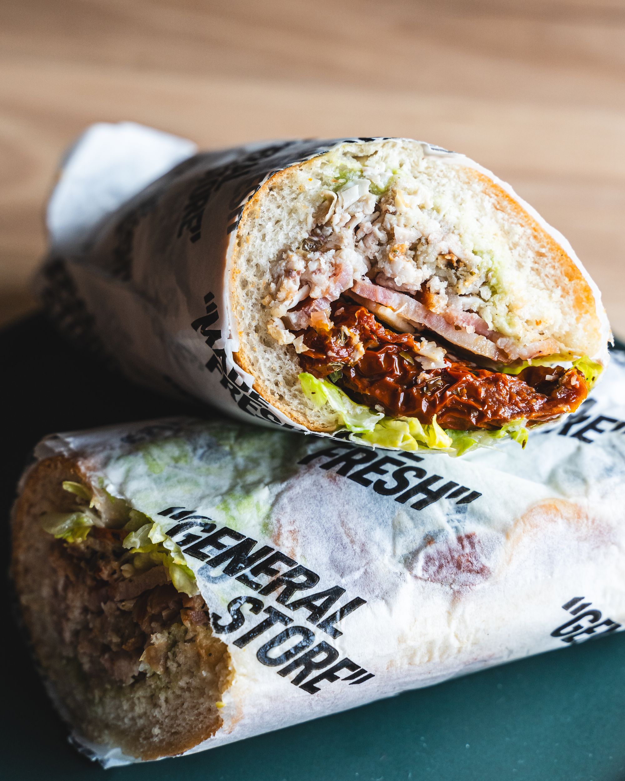 Close up cross section of sandwich roll showing cheese, chicken, avocado, lettuce and sundried tomatoes