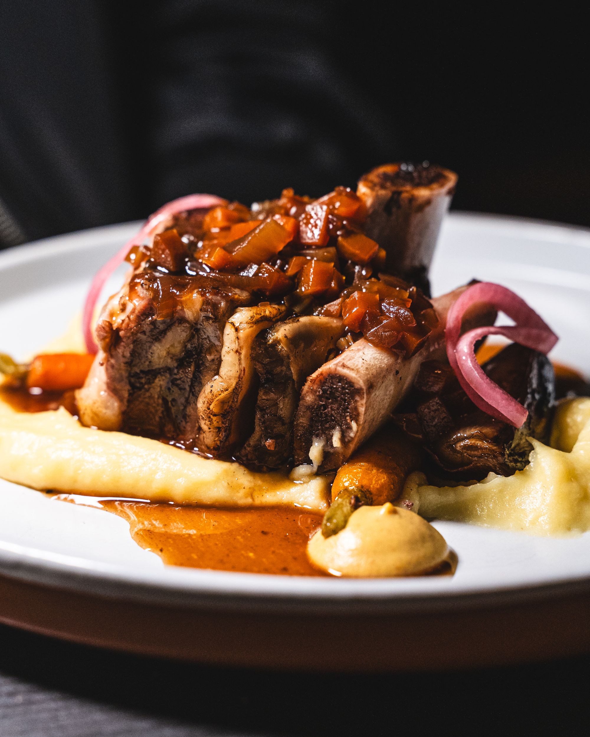 Close up of beef short rib with jus, sitting on a bed of mashed potato