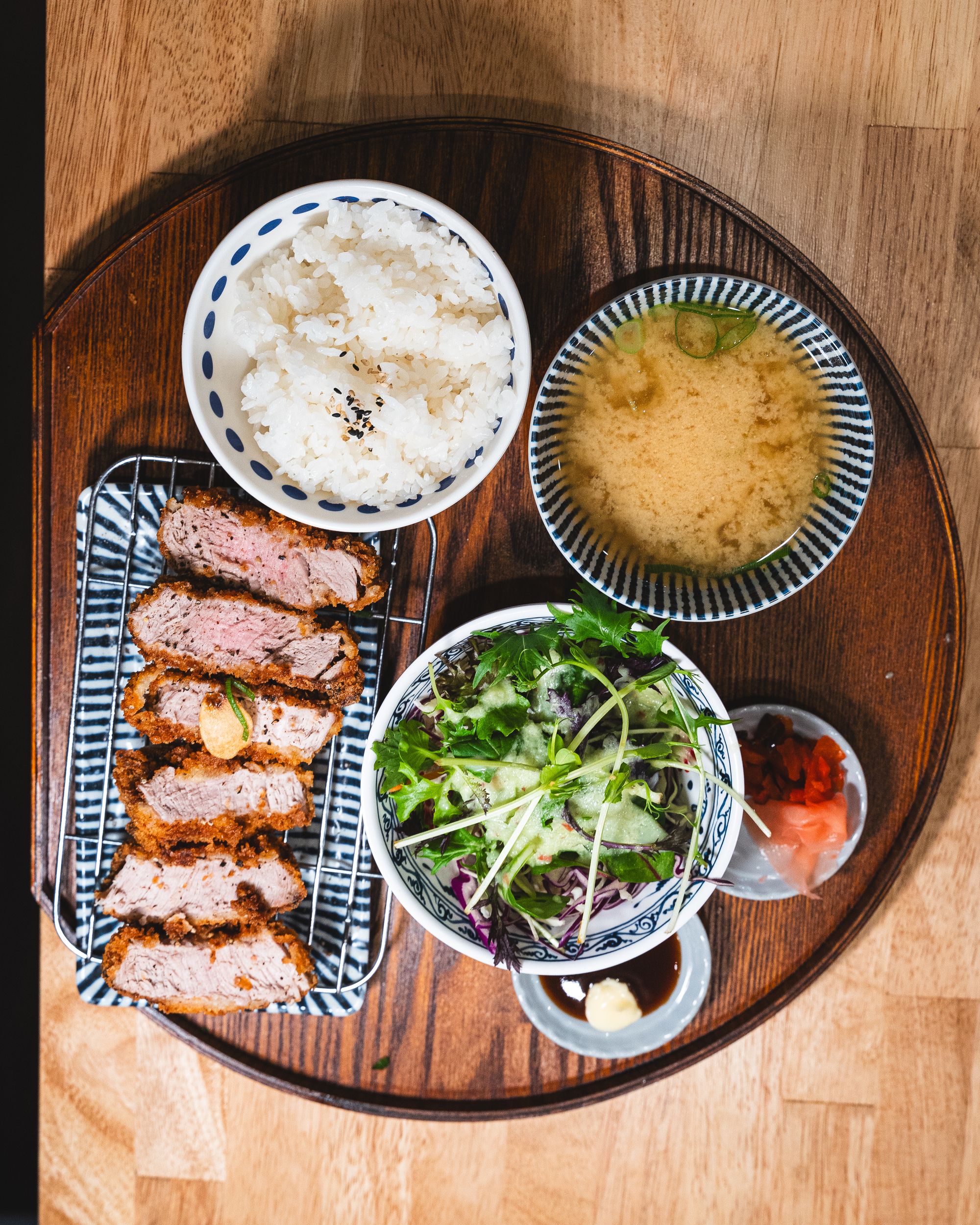 Top down shot of pork katsu, salad, pickled raddish, tonkatsu sauce, miso soup and rice served on a wooden tray
