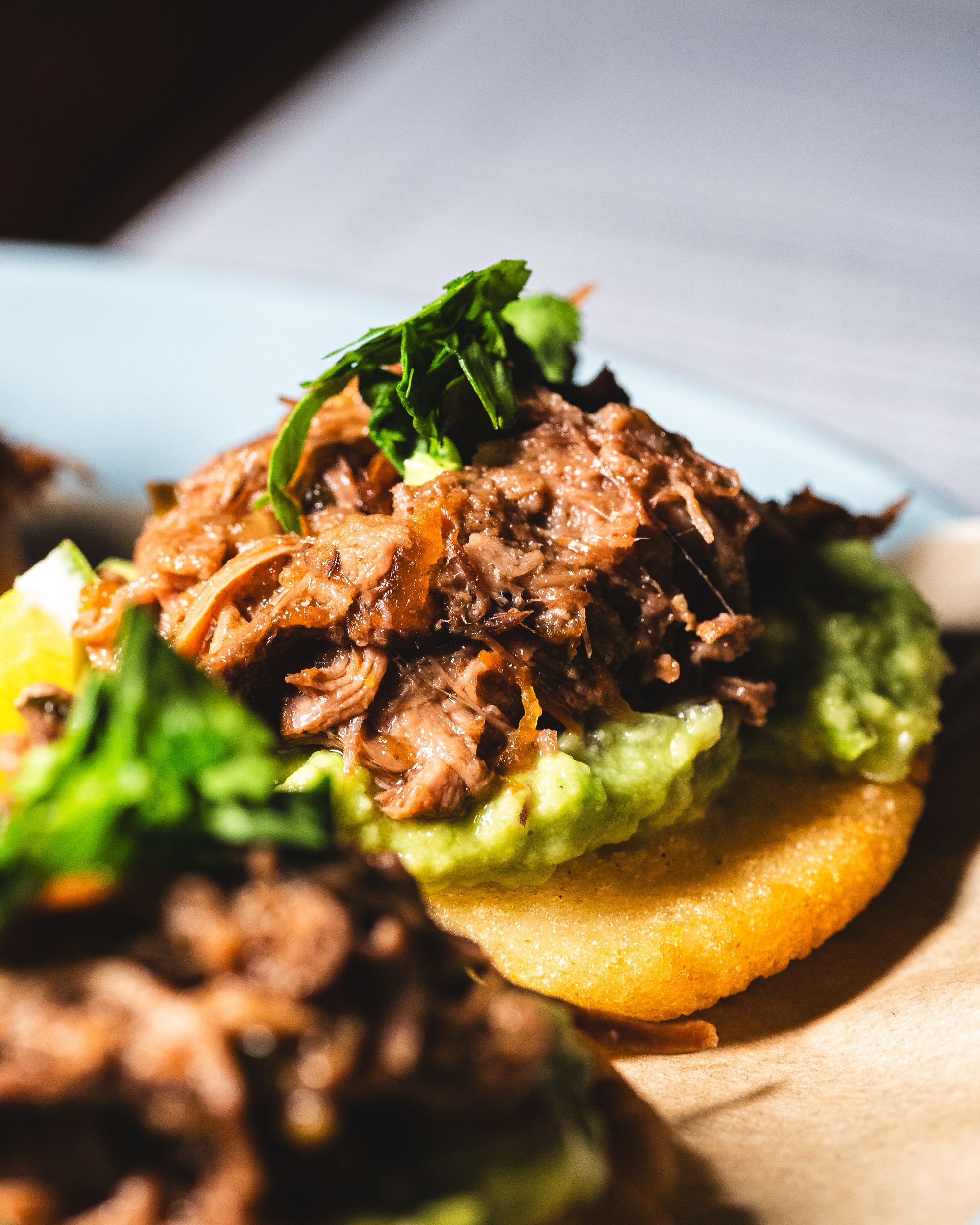 Close up of braised ox tail on an arepa with aji and salsa