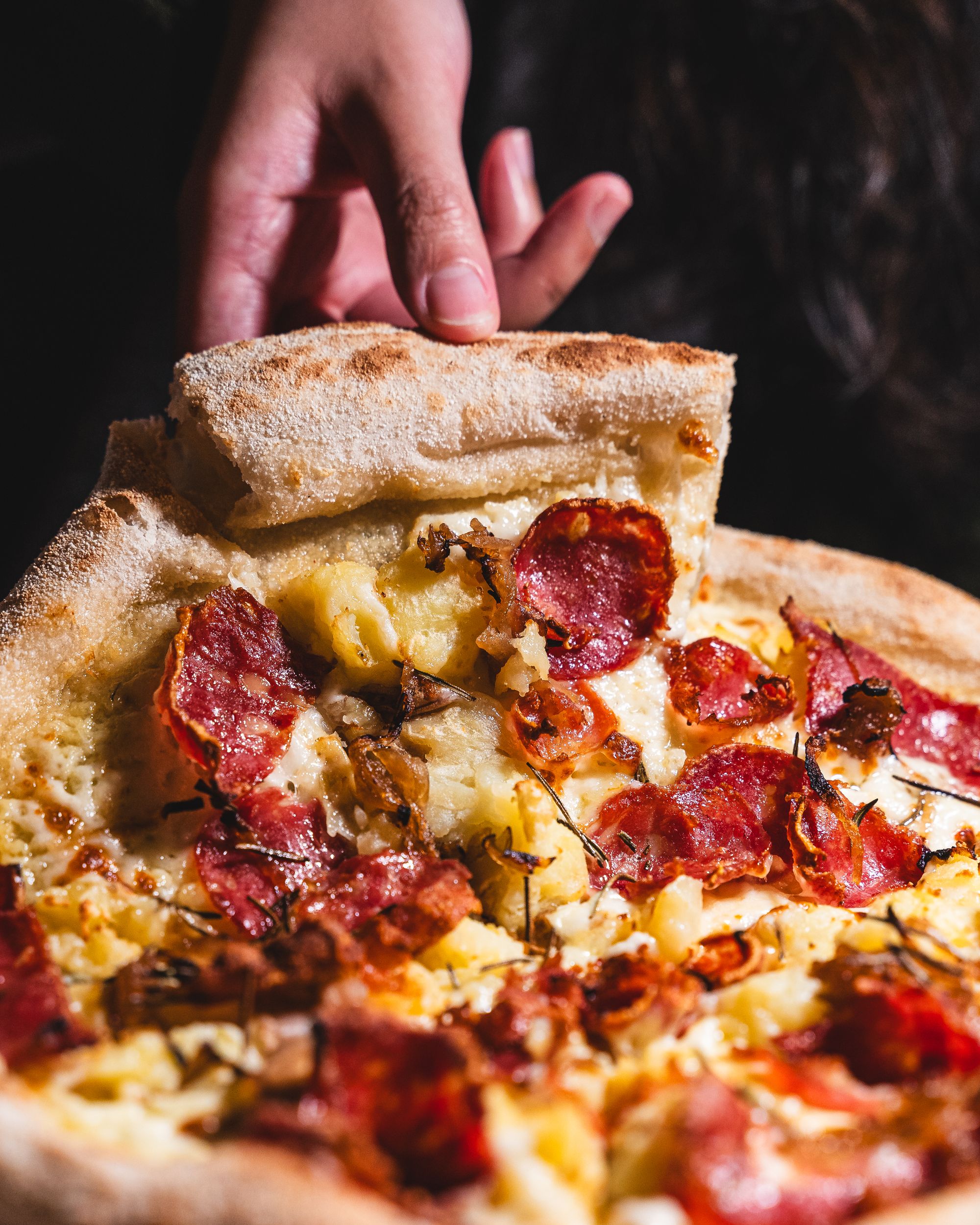 Hand picking up a slice of pizza with pepperoni