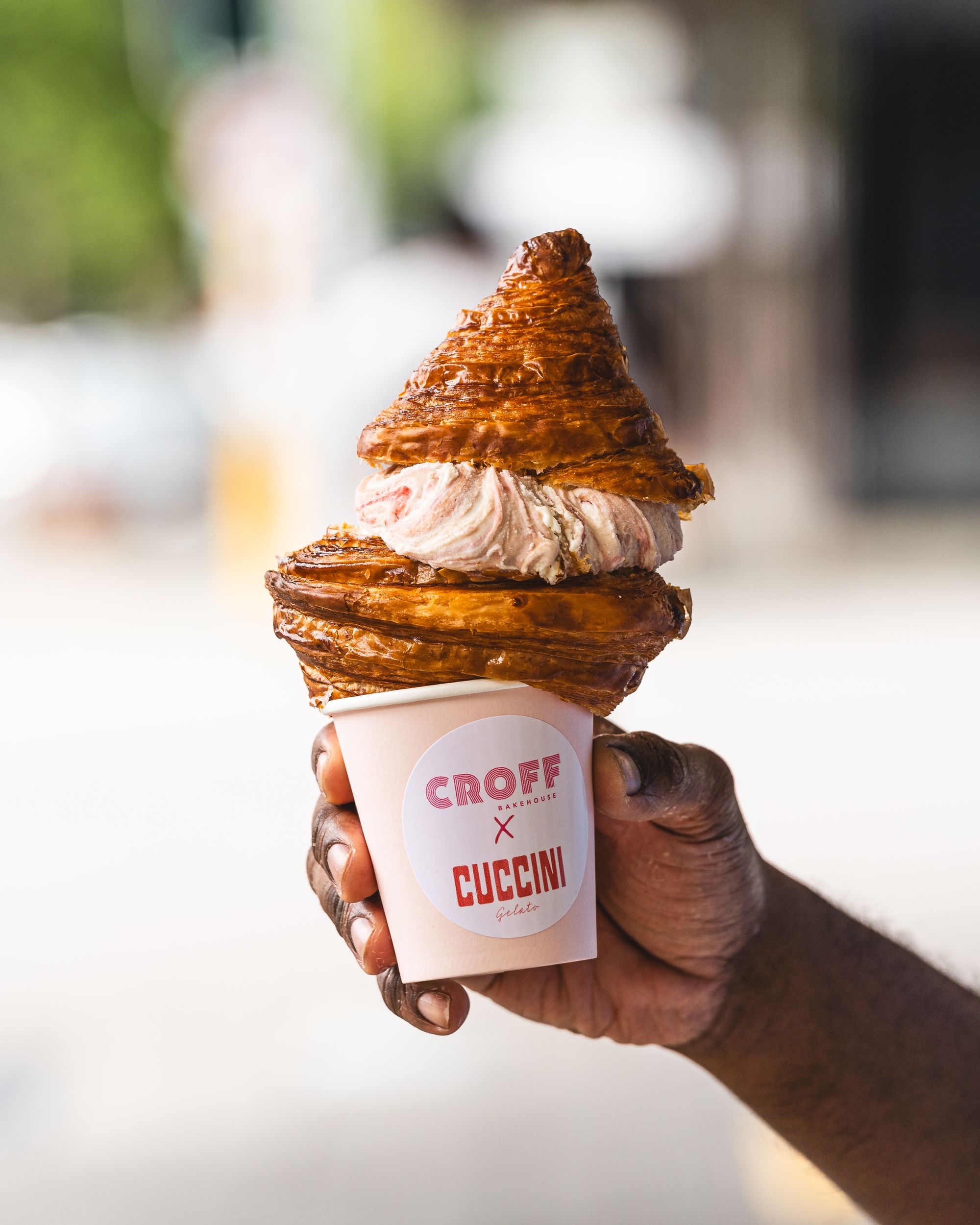 Hand holding a croissant cut in half with strawberry ice-cream wedged in-between