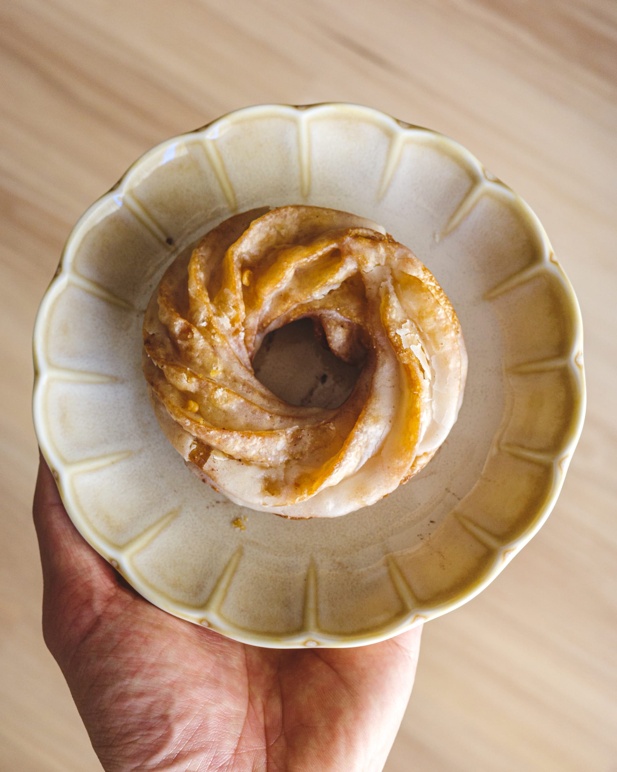 Top down shot of hand holding a cruller donut on a circular plate