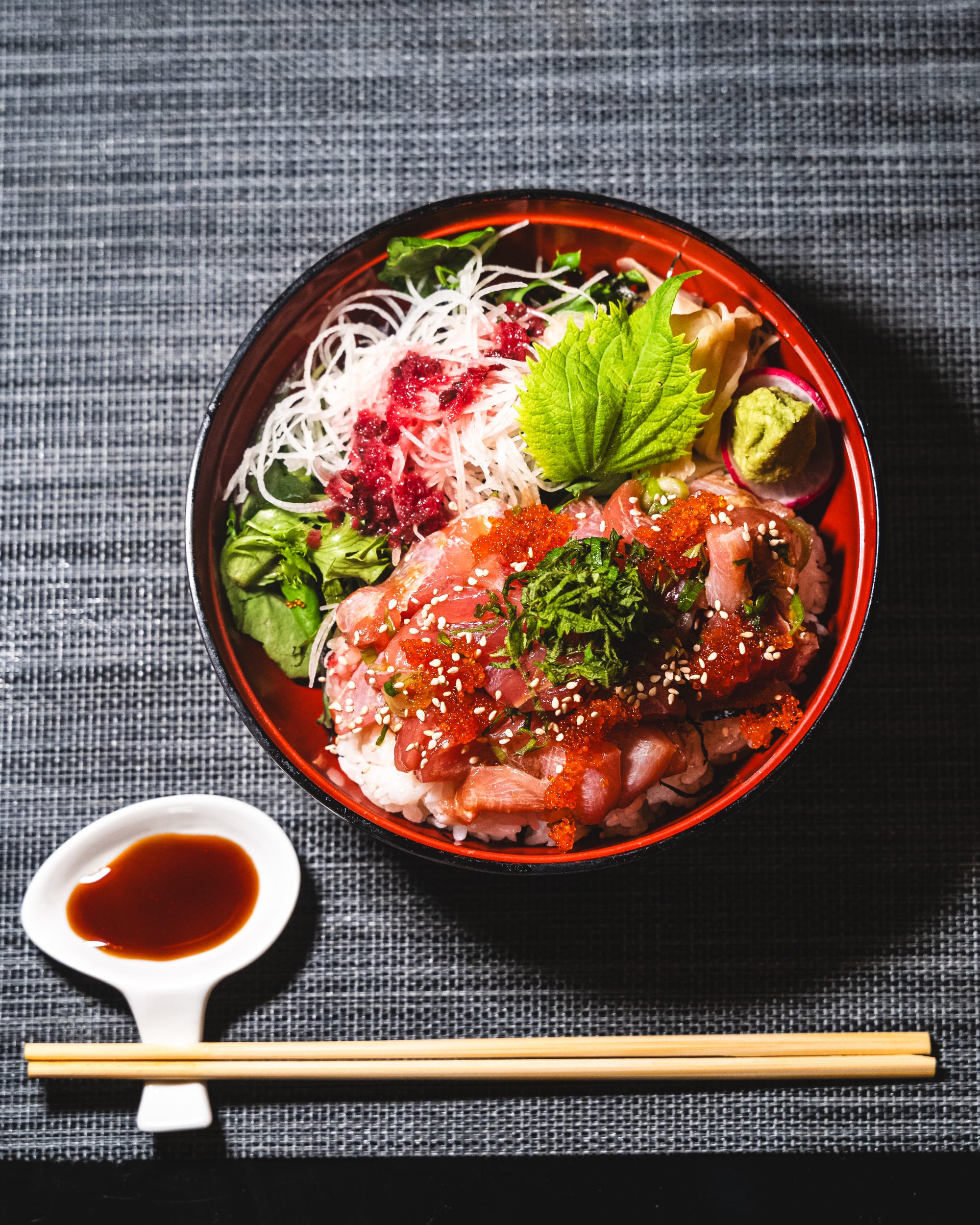 Top down shot of tuna sashimi on a bed of rice with a shiso leaf and salad
