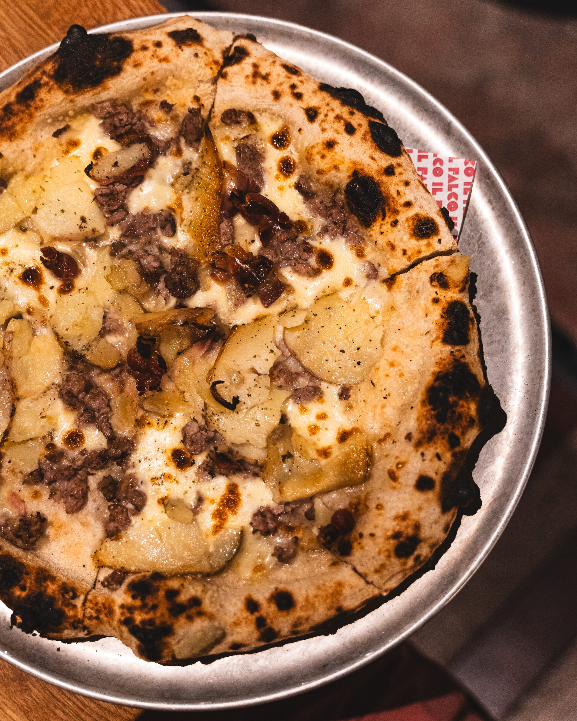 Top down shot of pizza with potato, guanciala, pork sausage and herbs