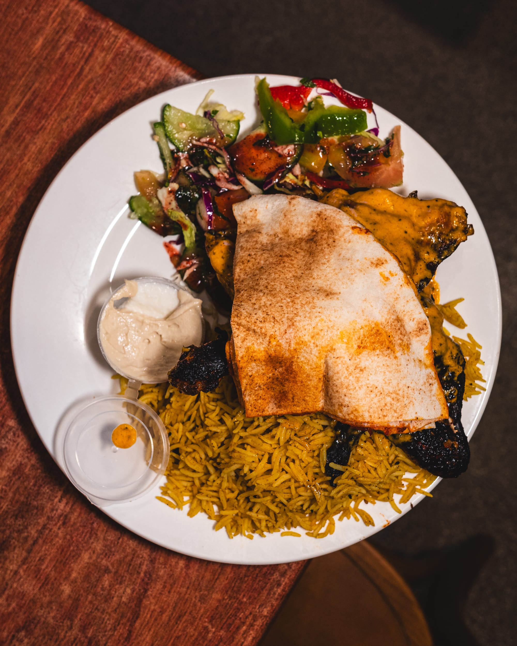 Top down shot of grilled chicken with hommus, garlic dip, Lebanese bread, salad and biriyani rice