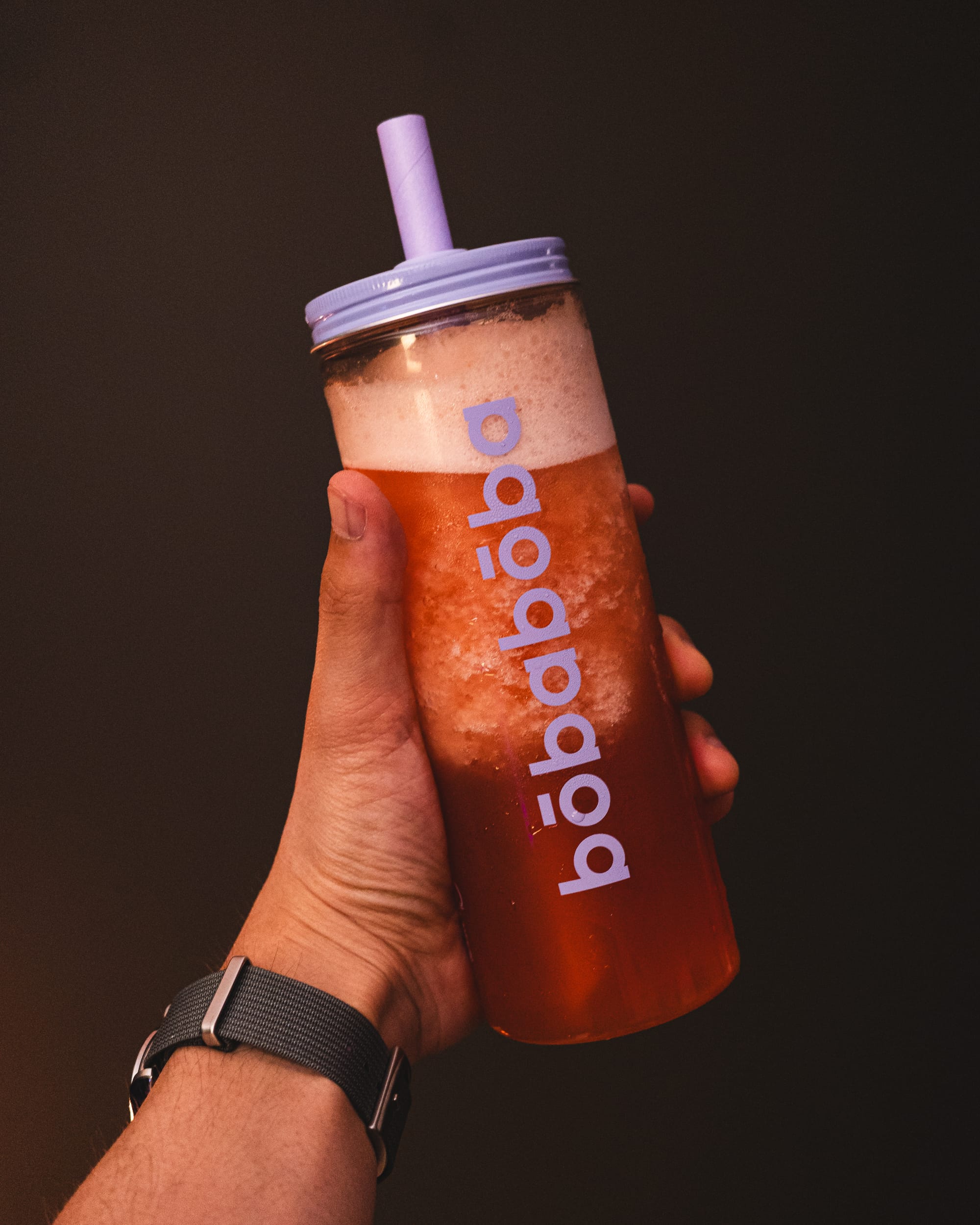 Hand holding plastic bottle with Bobaboba written in it, filled with a crushed guava drink