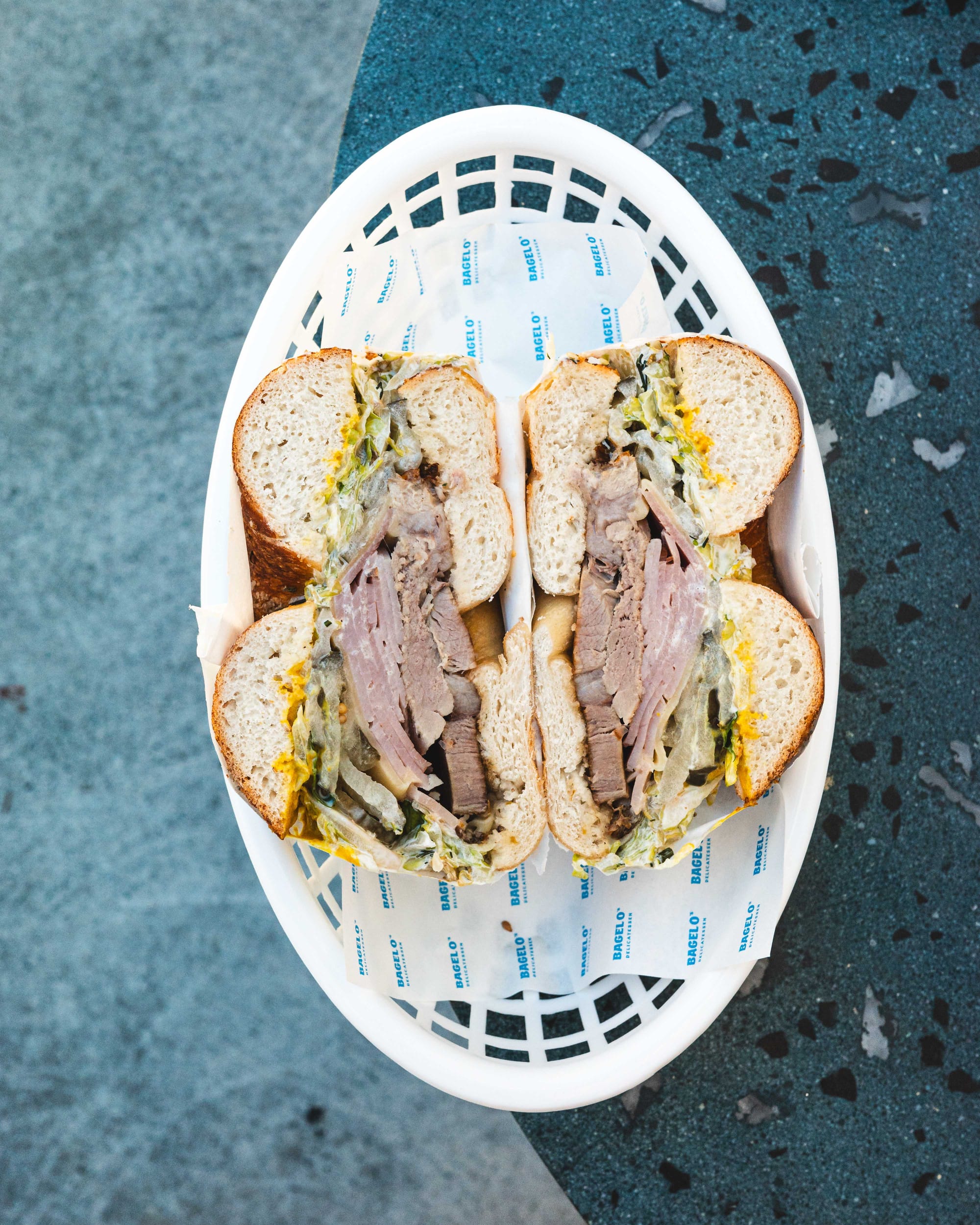 Top down shot of bagel with roast pork, ham, cheese, pickles, mustard, lettuce and dill