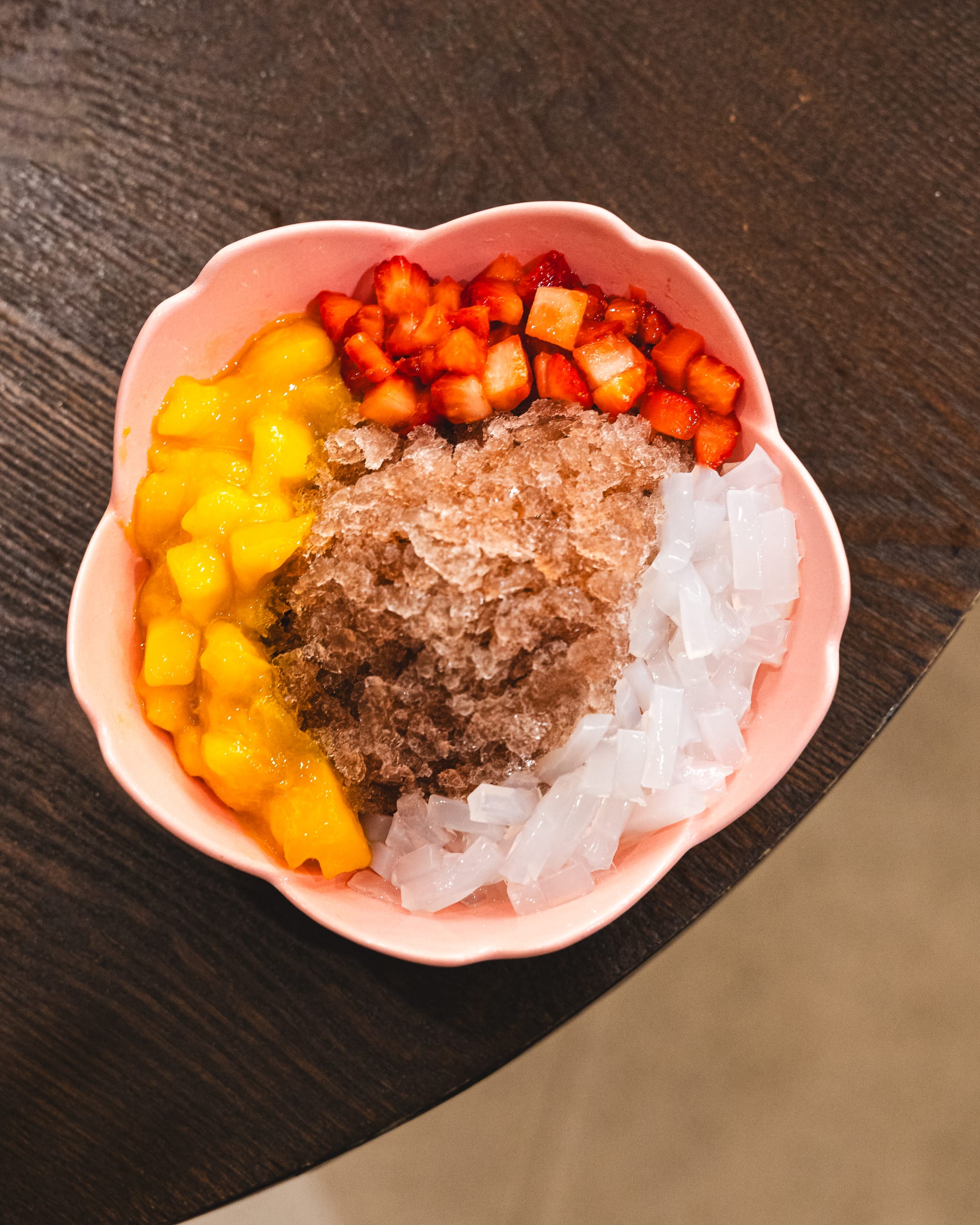 Top down shot of crushed ice and cubed mango, strawberry and lychee jelly in a flower shaped bowl