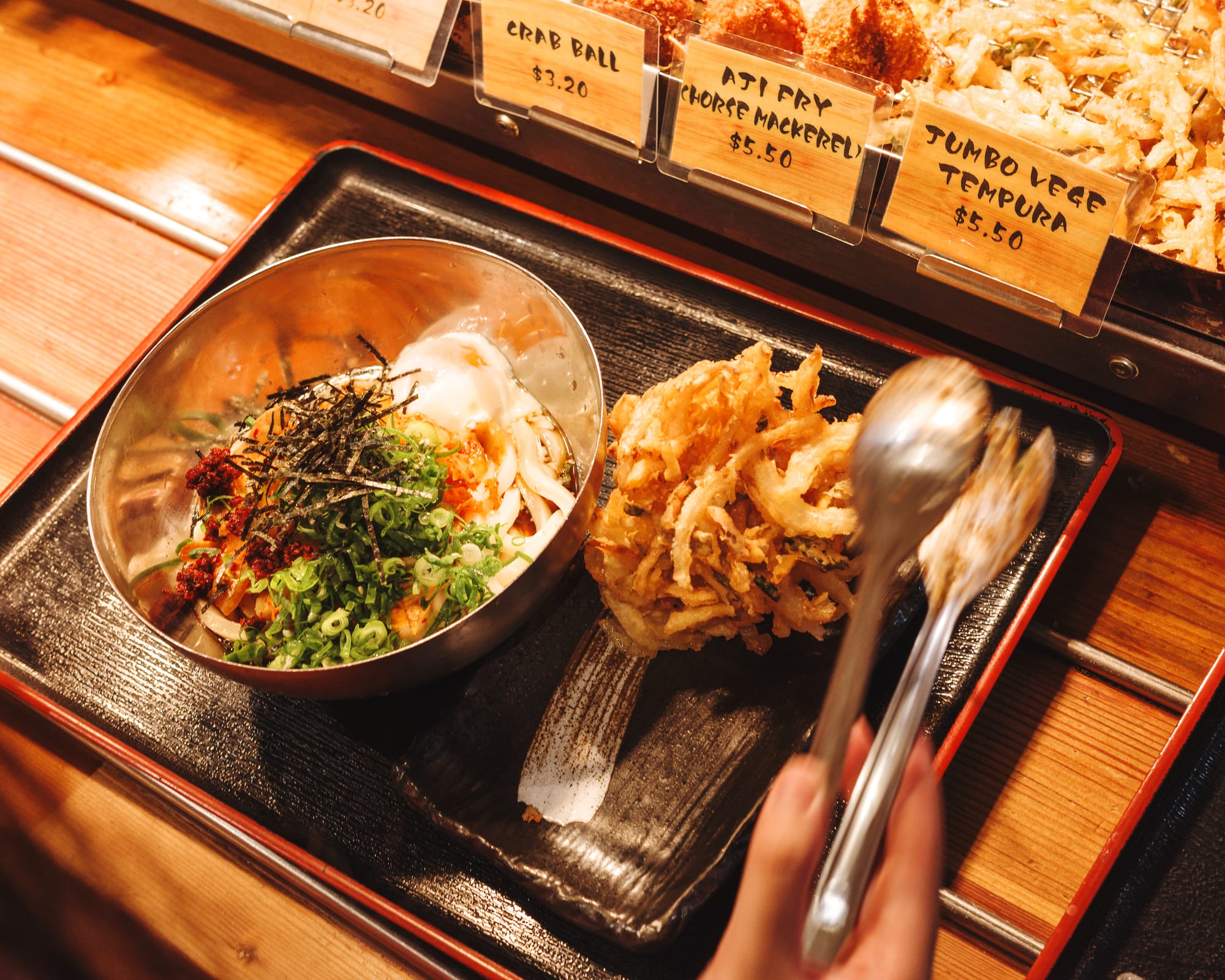 Hand holding tongs reaching for vegetable tempura 