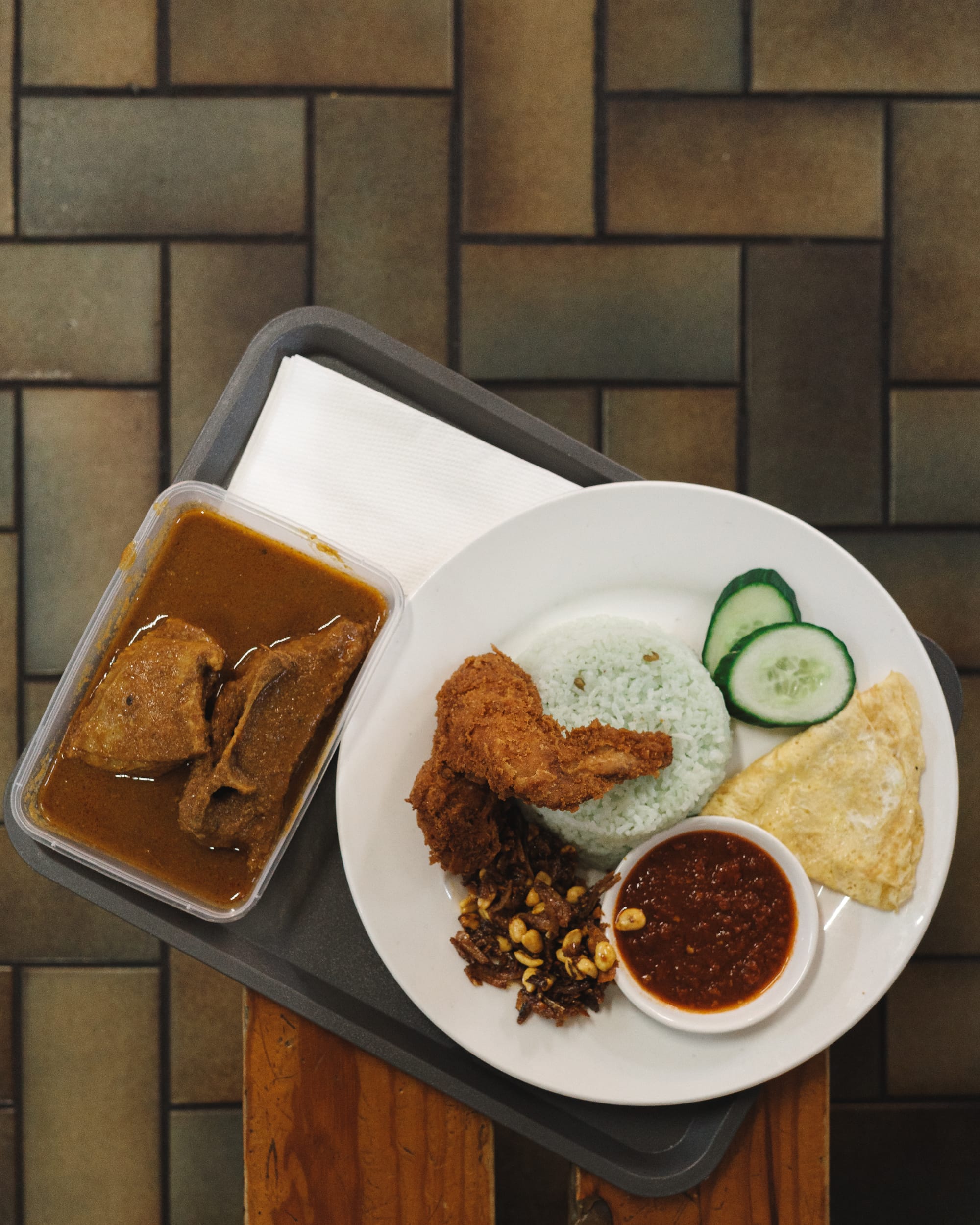 Top down shot of rice, chicken, egg, cucumber and sambal with a side of curry