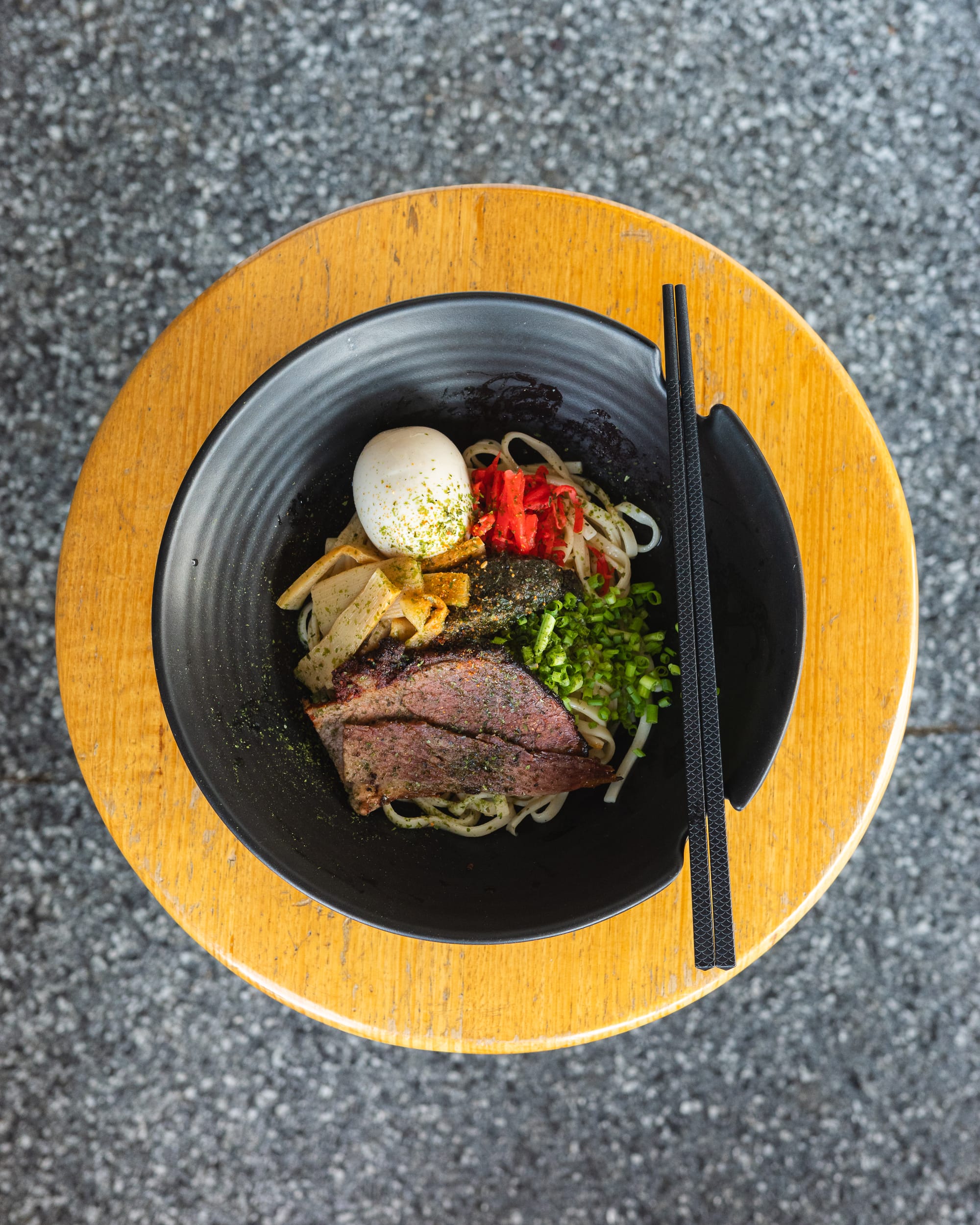 Top down shot of noodles with egg, raddish, torched pastrami, green onions and bamboo shoots