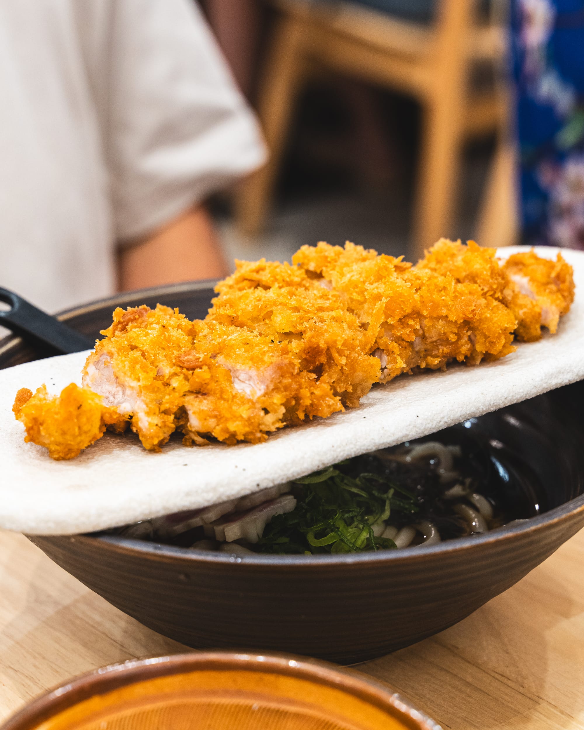 Plate of chicken katsu resting on top of a bowl of udon