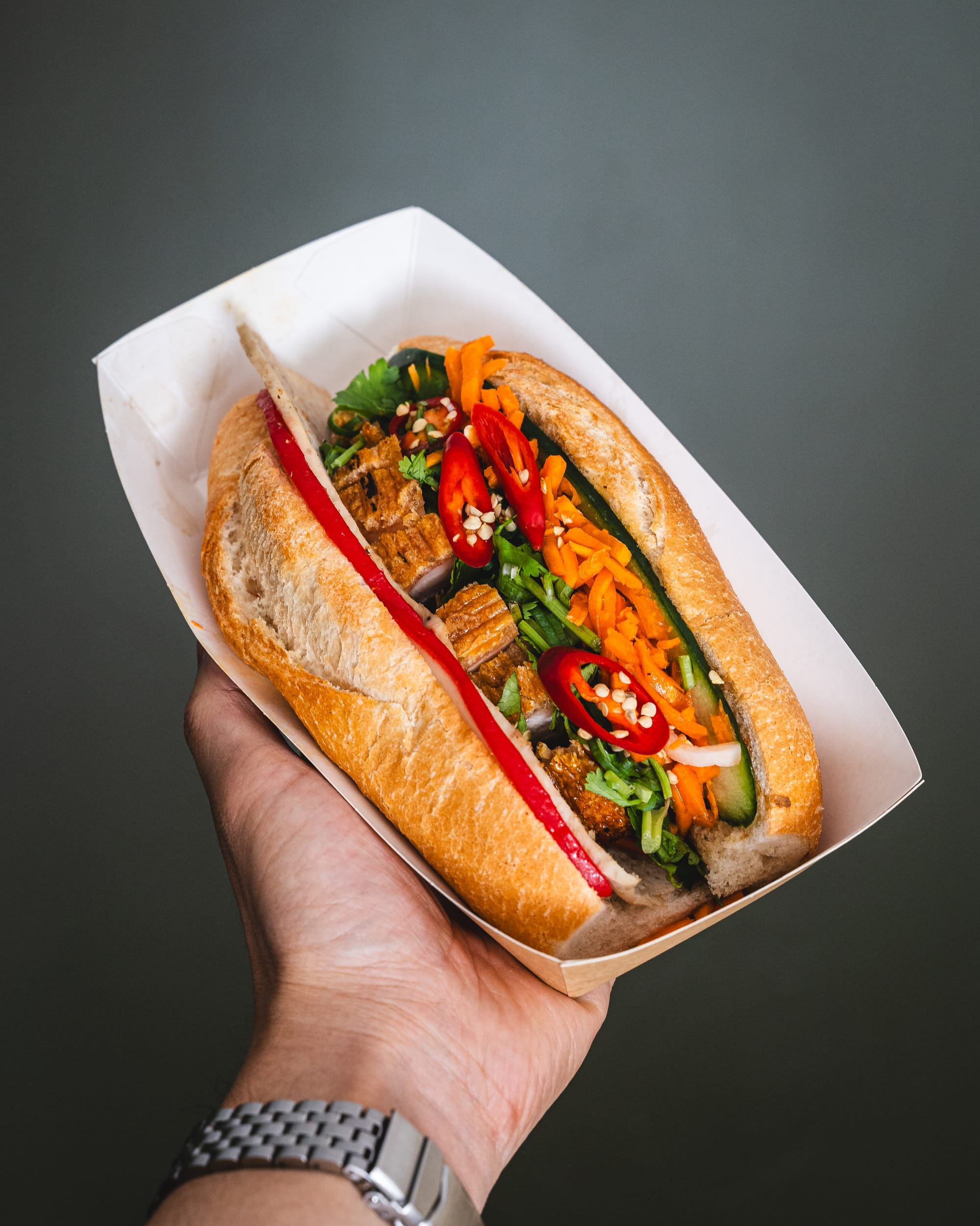 Hand holding banh mi against a wall