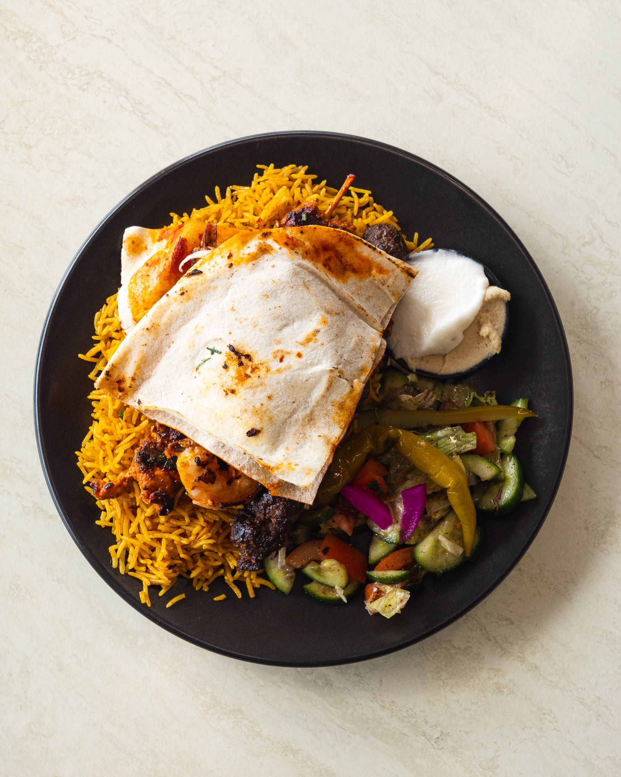 Top down shot of rice, Lebanese bread, hummus, garlic sauce, meat and salad on a plate