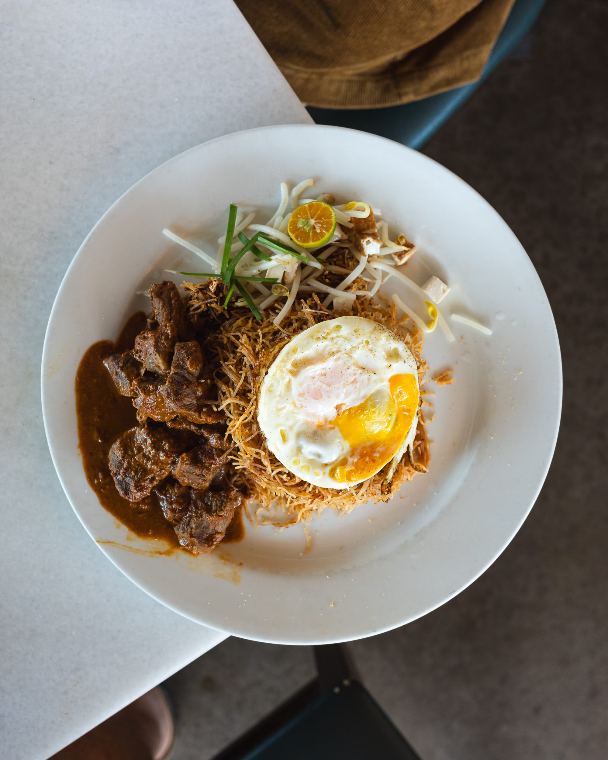 Top down shot showing lamb rendang, vermicelli noodles and fried egg
