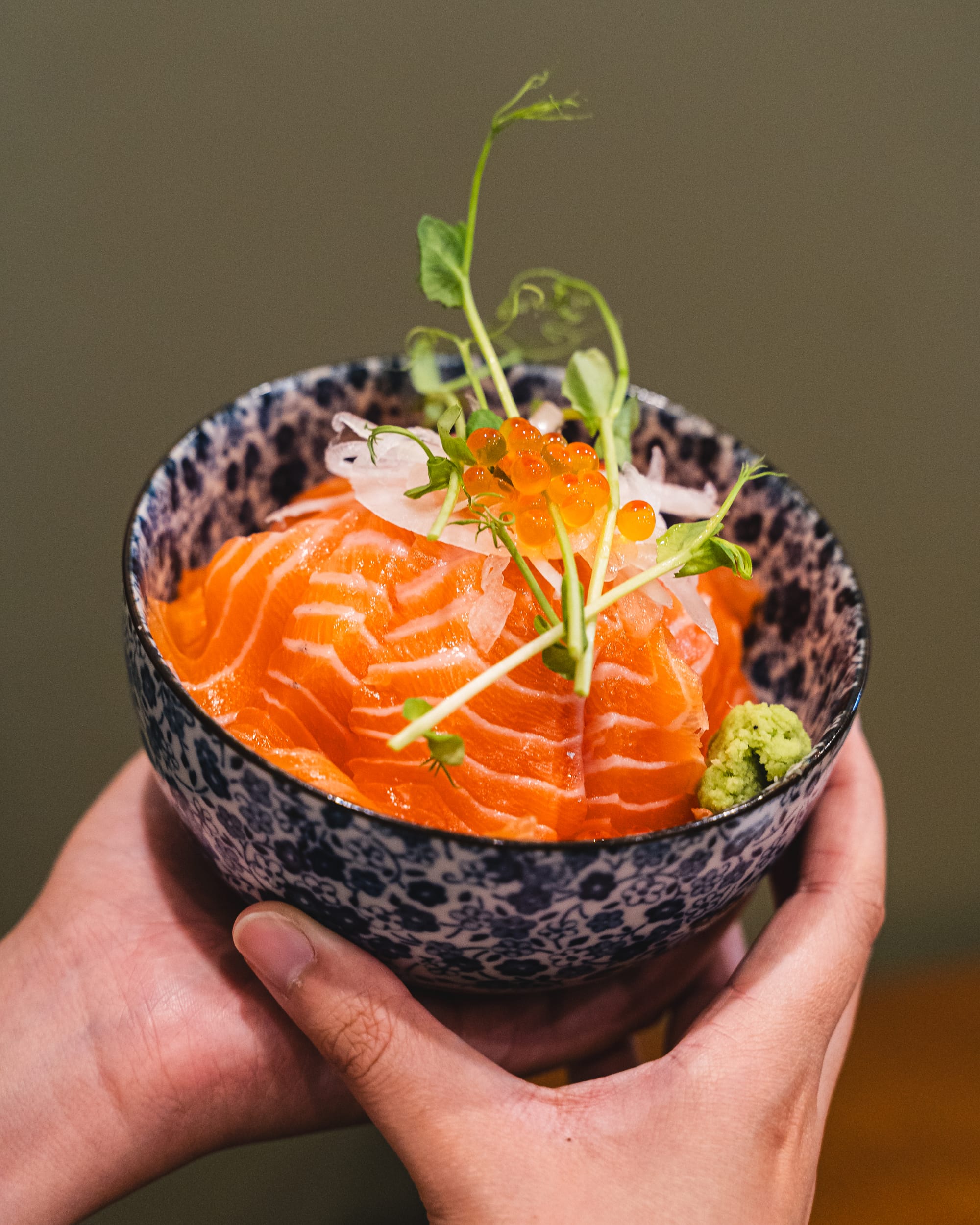 Hand holding a bowl with salmon sashimi and ikura
