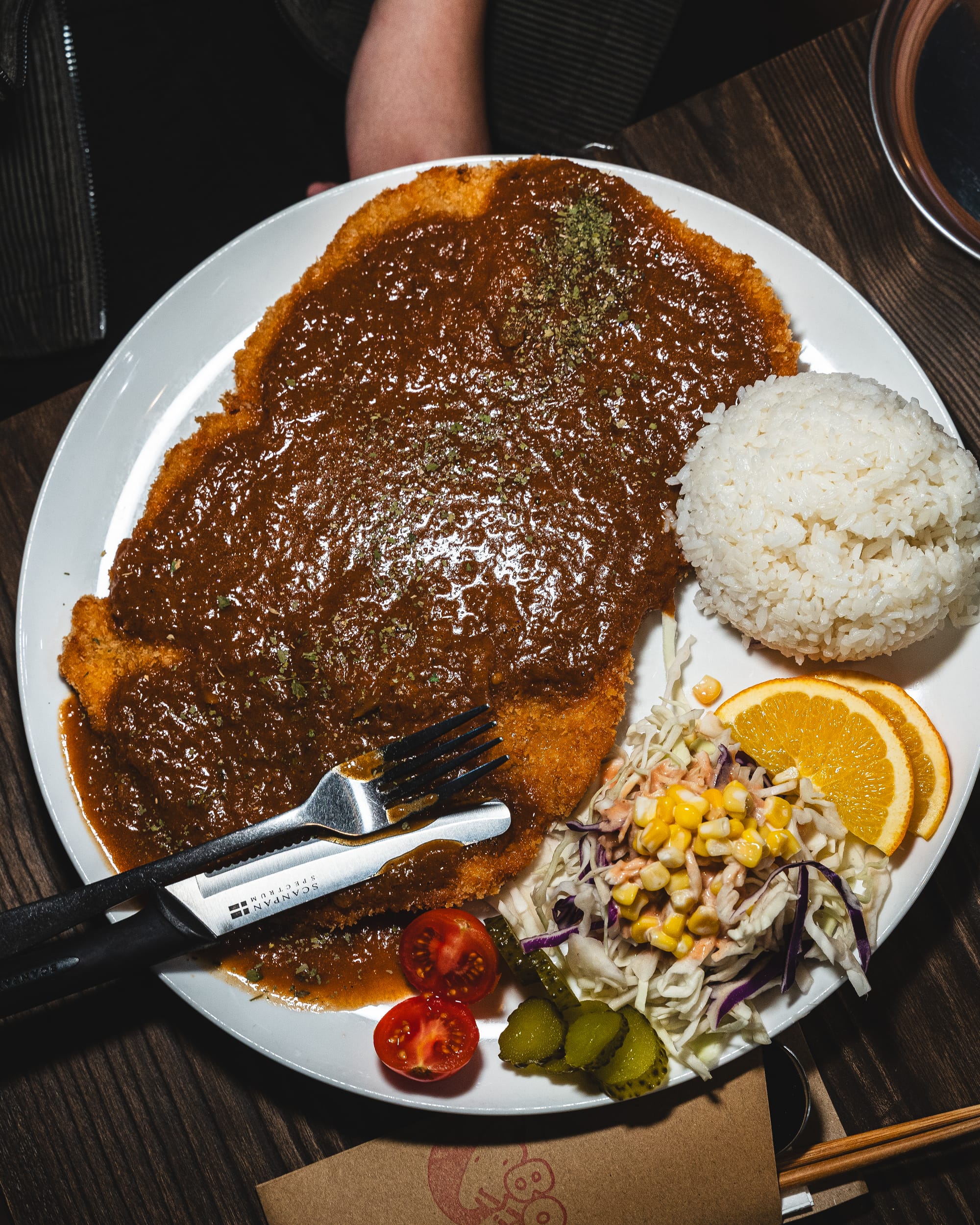 Top down shot of large fried pork cutlet with sauce, rice and salad