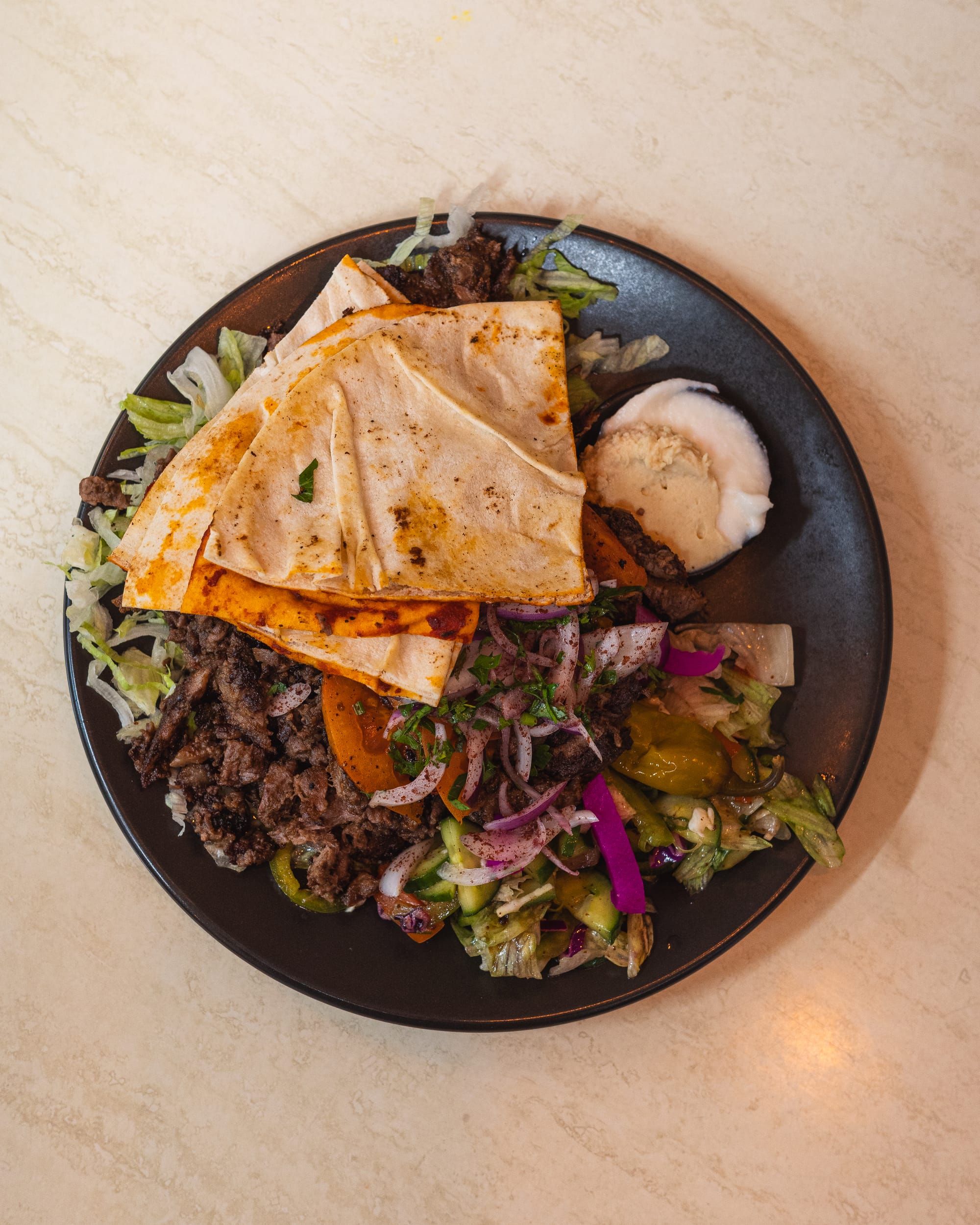 Top down shot of lamb shawarma with flatbread, hummus and garlic dip